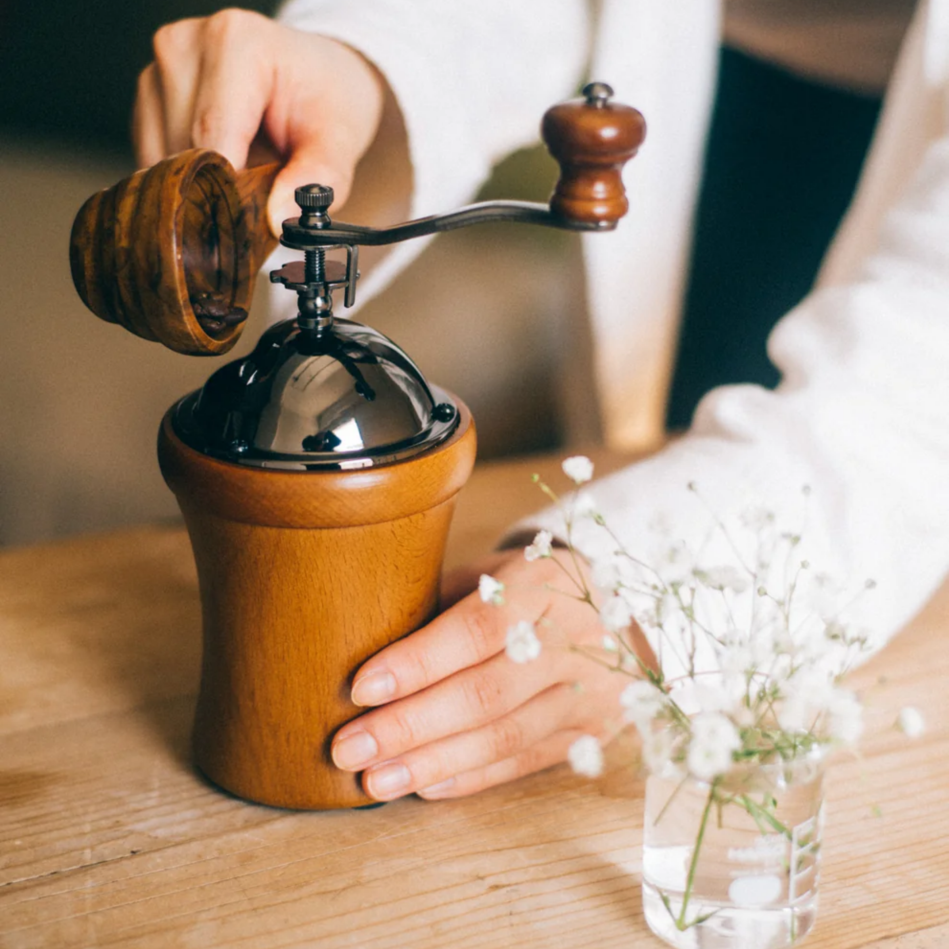 Shown adding a coffee inside Hario Dome Coffee Mill, natural wood finish with rounded body and tapered center for easy grip, featuring a hand crank with wood handle and ceramic burr for consistent manual grinding. Compact and rustic design, ideal for 35g of coffee grounds.