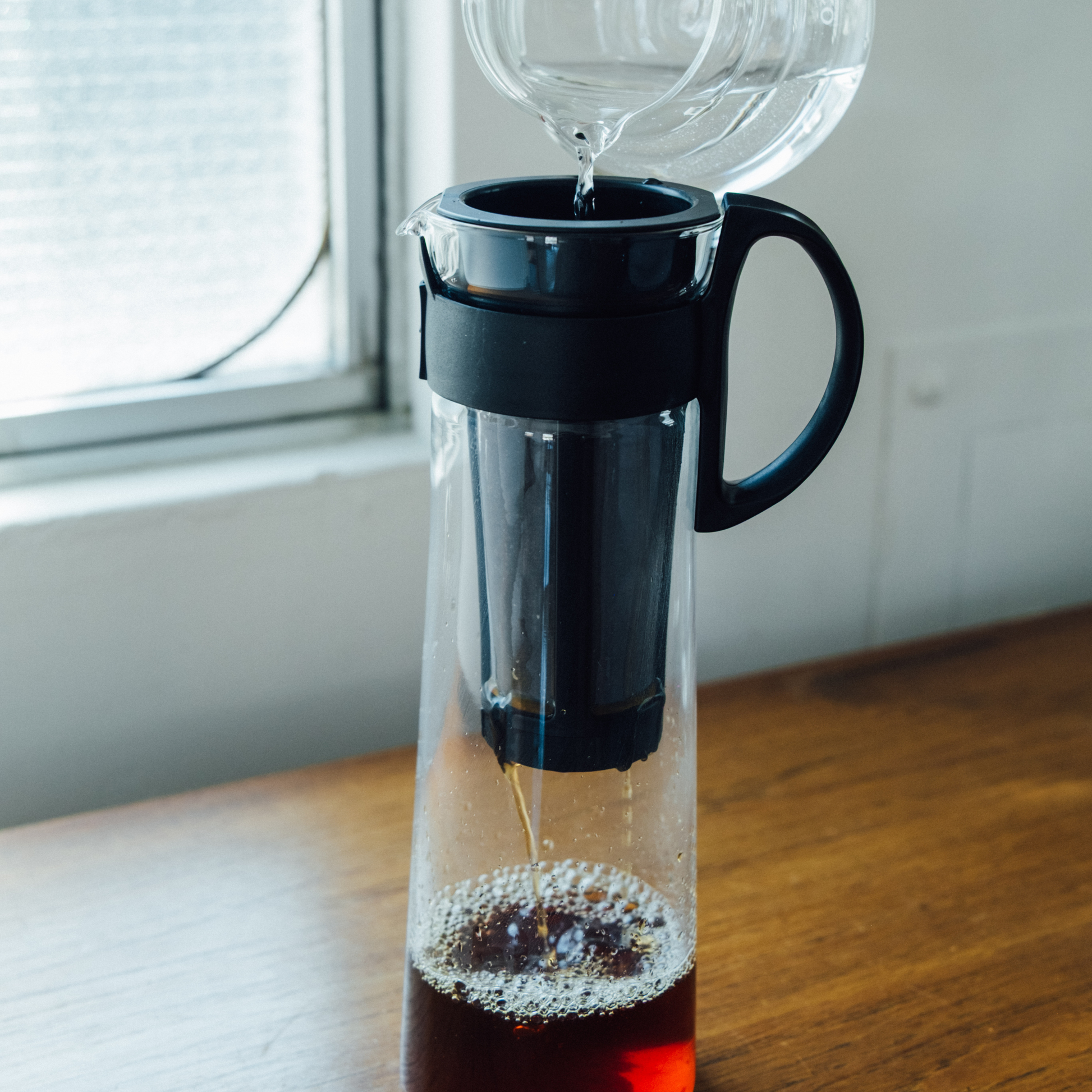 Pouring water inside the Hario Cold Brew Coffee Pot Glass Black that is made from durable heatproof Hario glass, foolproof design with 1L capacity.