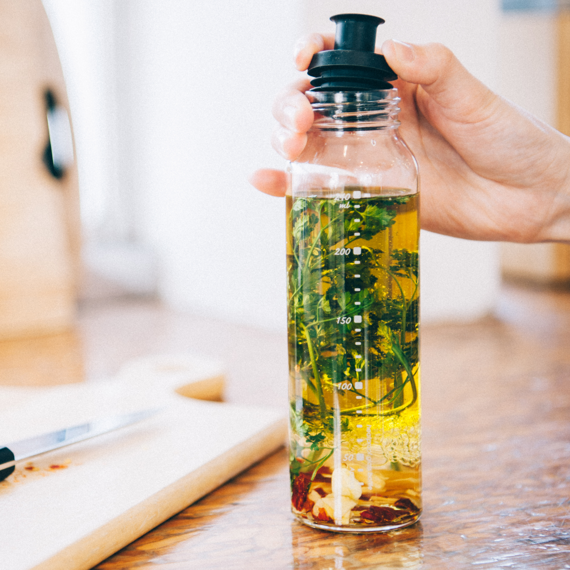 HARIO Dressing Bottle, 250mL capacity, shown with oil and spices inside, heatproof glass with twist cap and modest pouring spout, available in Pale Grey and Black. Designed for shaking, pouring, and storing homemade dressings; dishwasher and heat sterilization safe.