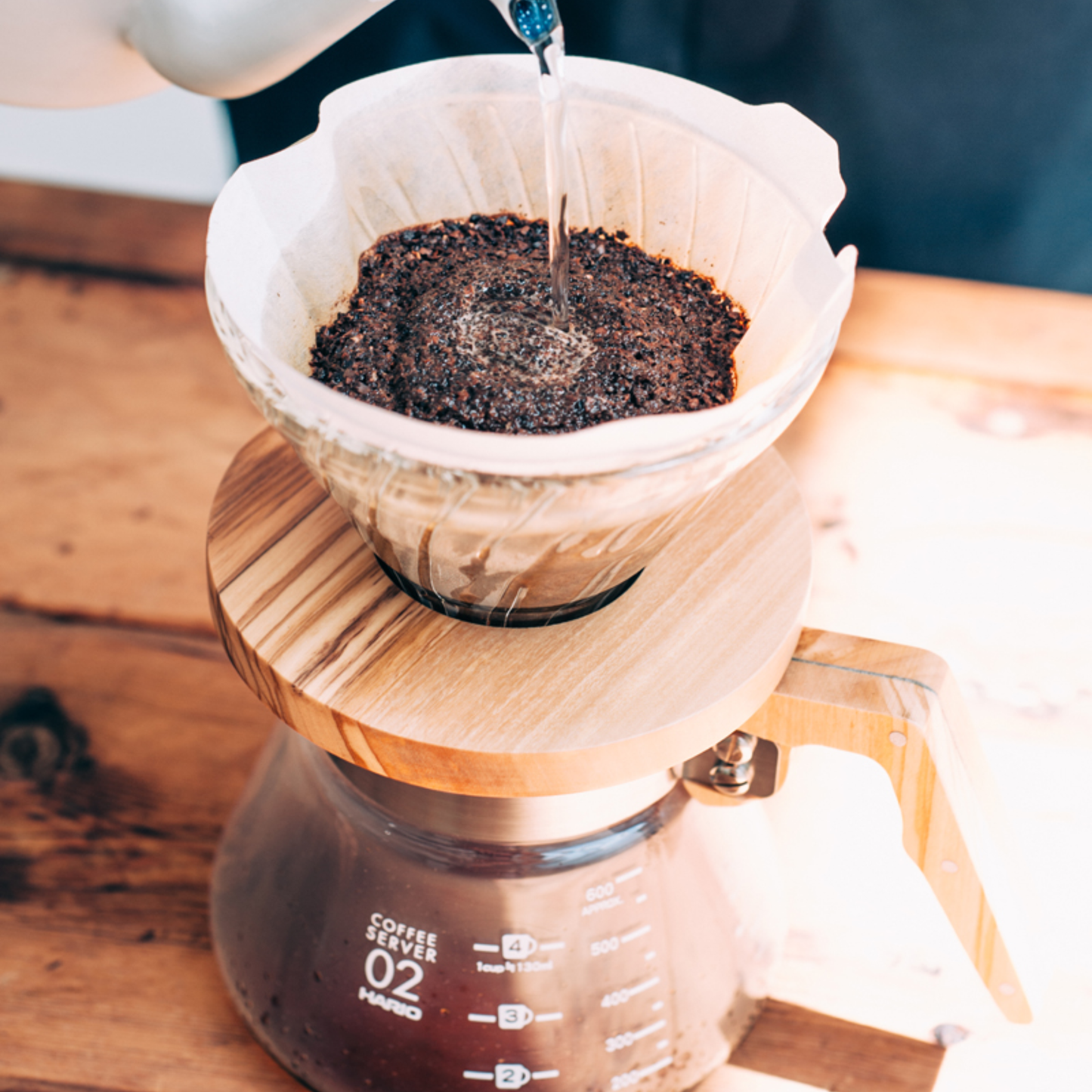 Dripping coffee straight to the Hario Glass Coffee Server 600 ml Olive Wood which includes pot from heatproof glass, lid from olive wood, handle, band and screw from stainless steel, with brass screw, featuring natural wood making each piece unique.