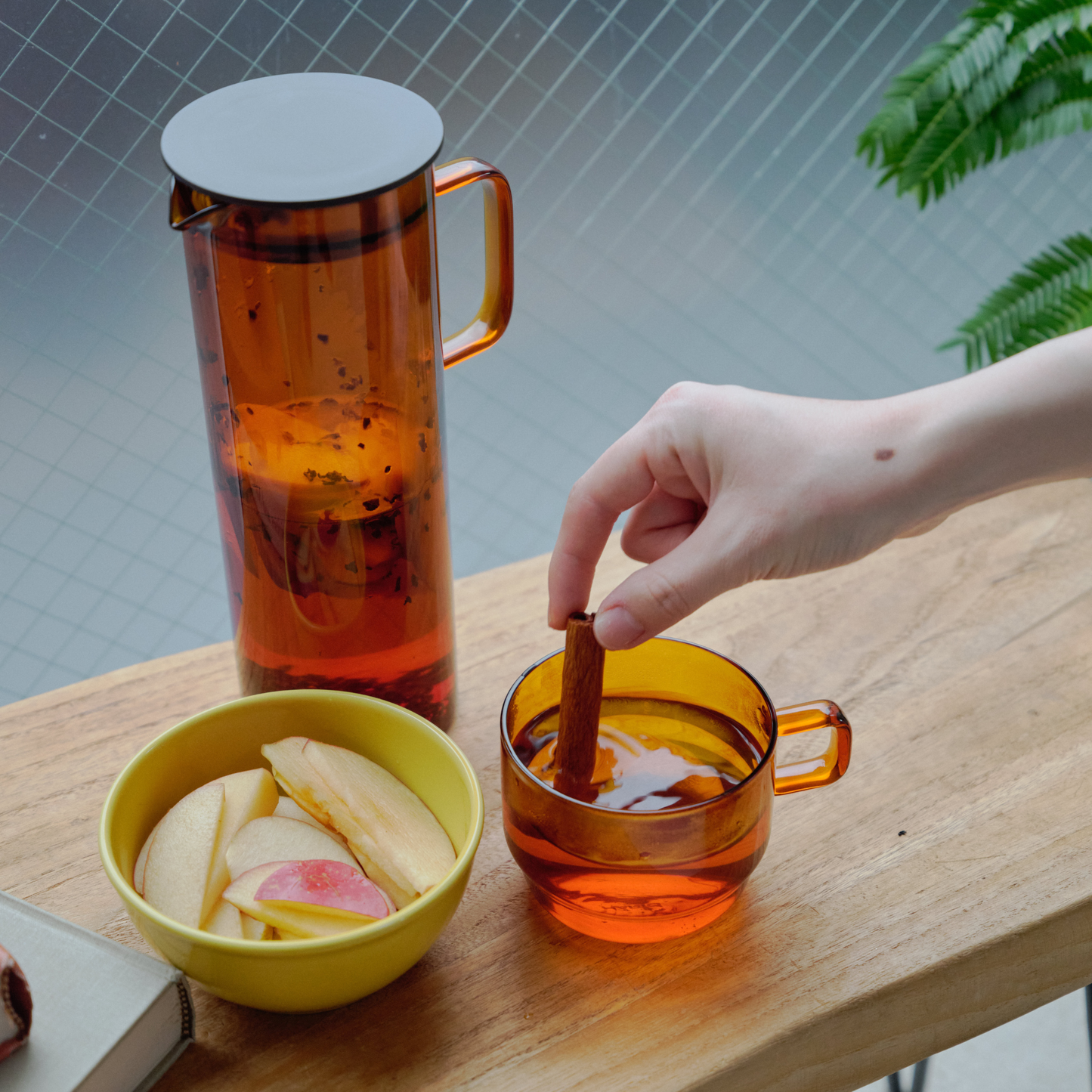 On a wooden table with Hario Glass Pitcher Amber that is made from heatproof glass with 800ml capacity, with a lid that has a mesh filter.