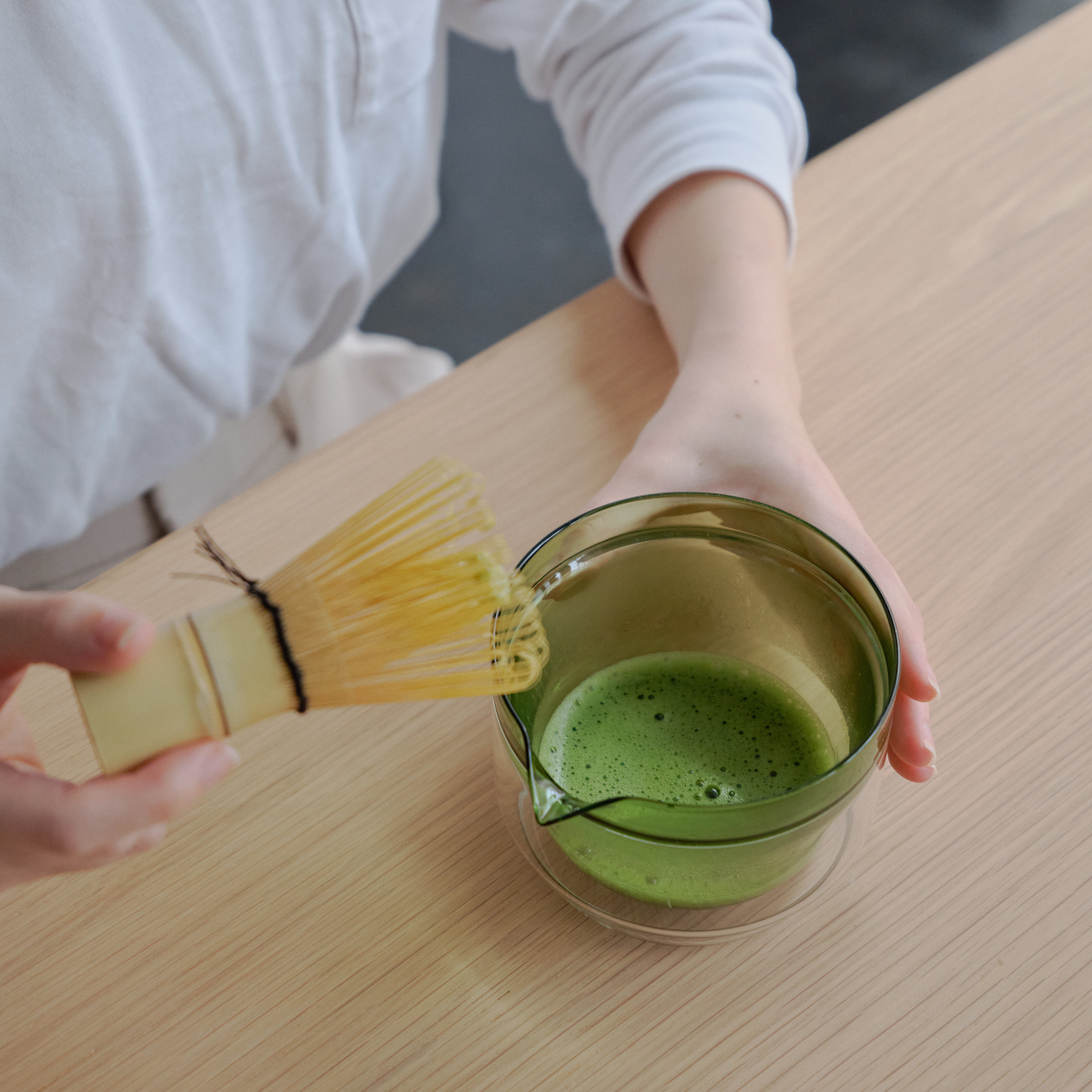 Showing the whisk and the bowl with the matcha, both items from the Hario Matcha Tea Set Green which includes a double-walled Matcha Bowl, stand from heatproof glass, Chasen or the whisk, chashaku or measuring spoon from bamboo and tea sifter from stainless steel.
