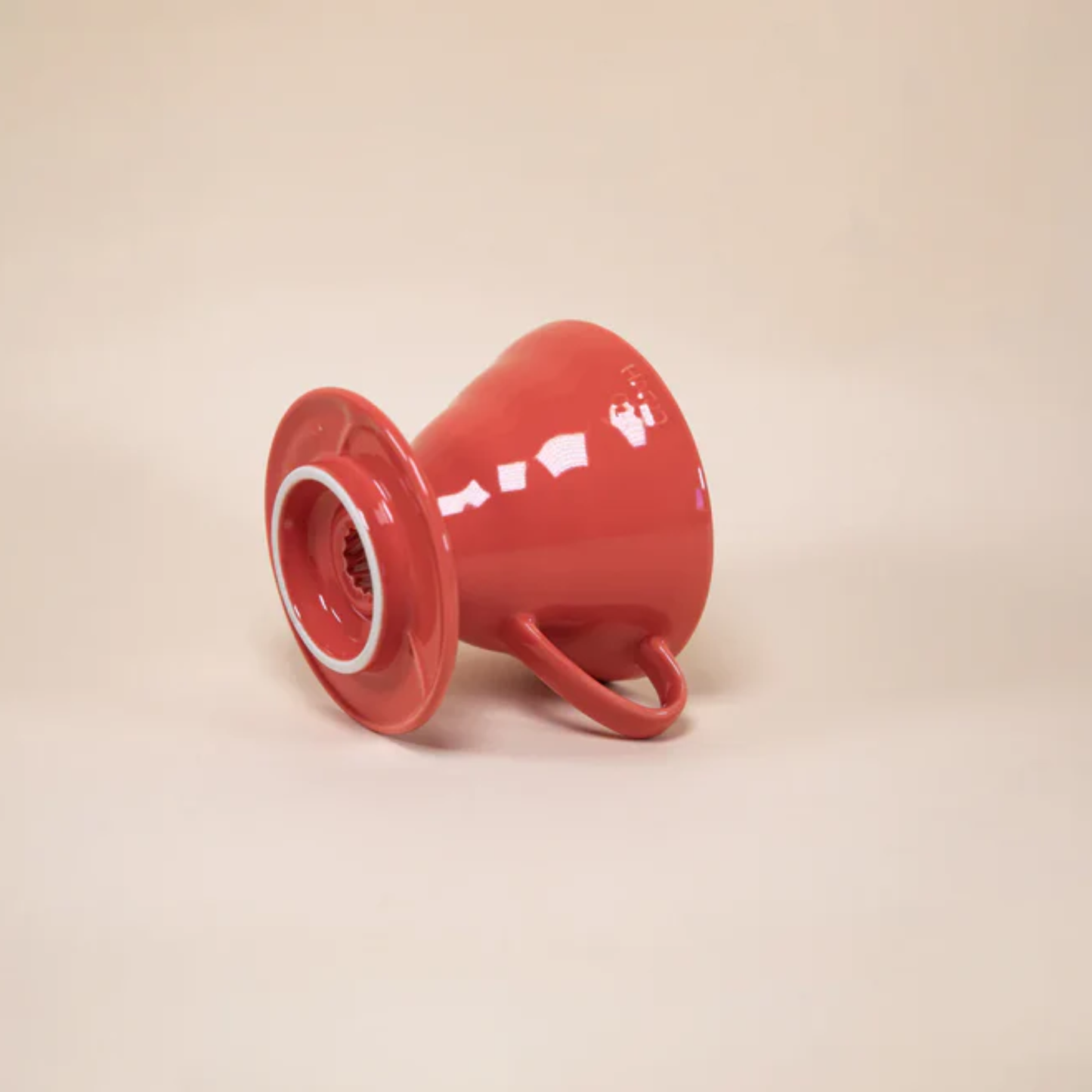 Laid and showing the bottom part of HARIO V60 ceramic coffee dripper red porcelain with spiral ridges and conical shape for adjustable brewing flow, includes polypropylene measuring spoon.