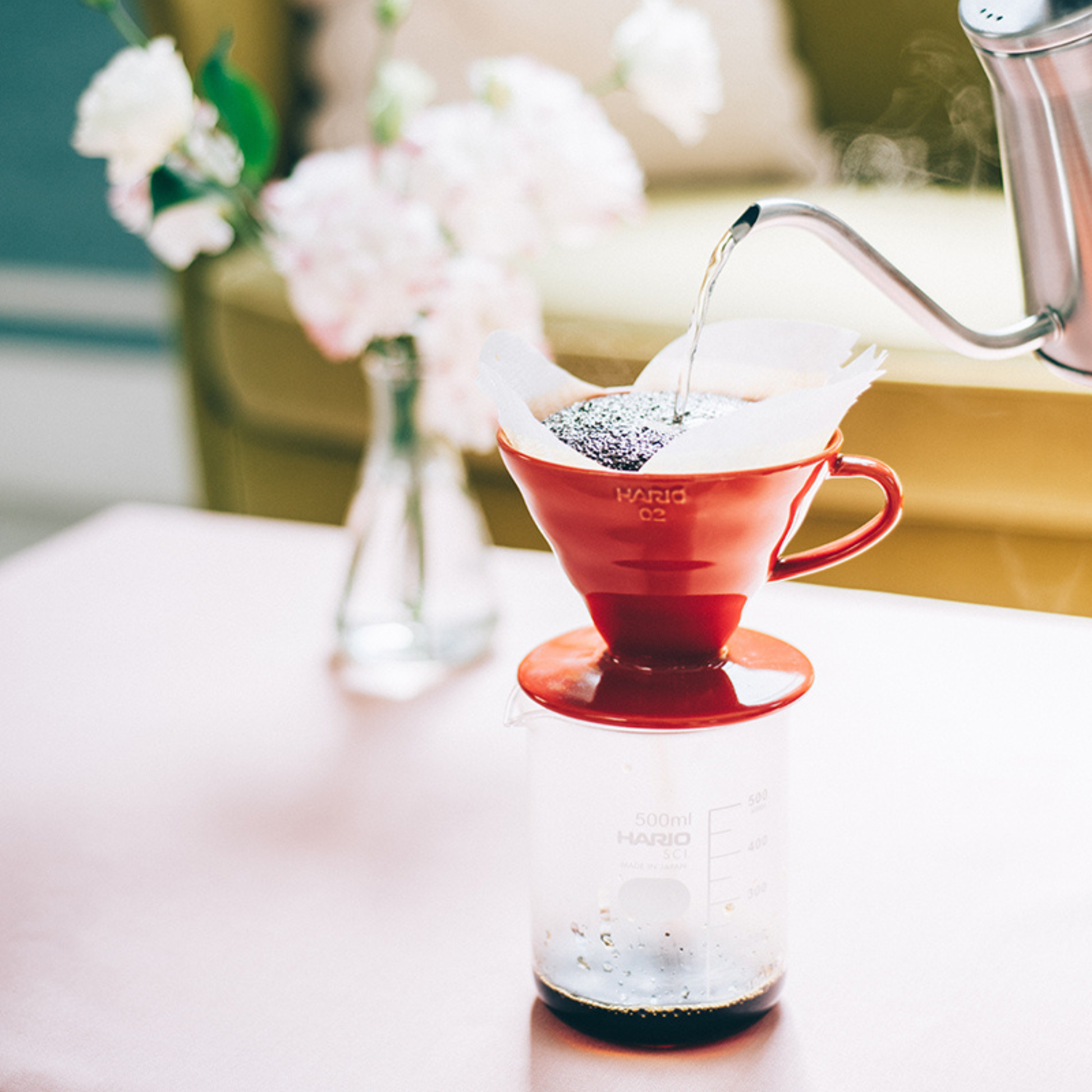 Hot water being poured in to and dripping coffee from HARIO V60 ceramic coffee dripper red porcelain with spiral ridges and conical shape for adjustable brewing flow, includes polypropylene measuring spoon.