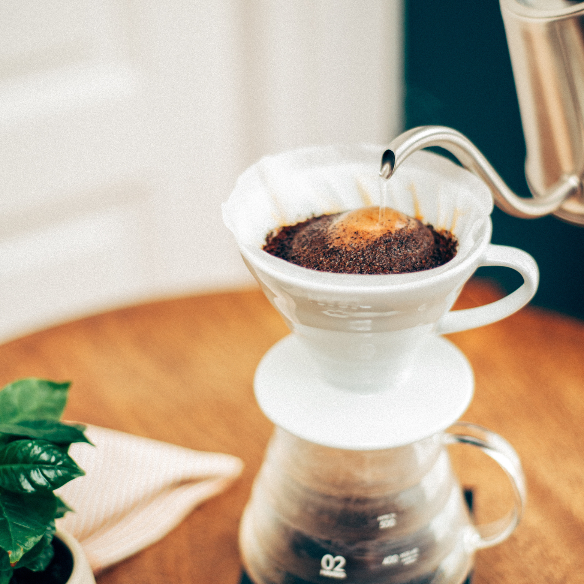 Hot water being poured in to and dripping coffee from HARIO V60 ceramic coffee dripper white porcelain with spiral ridges and conical shape for adjustable brewing flow, includes polypropylene measuring spoon.