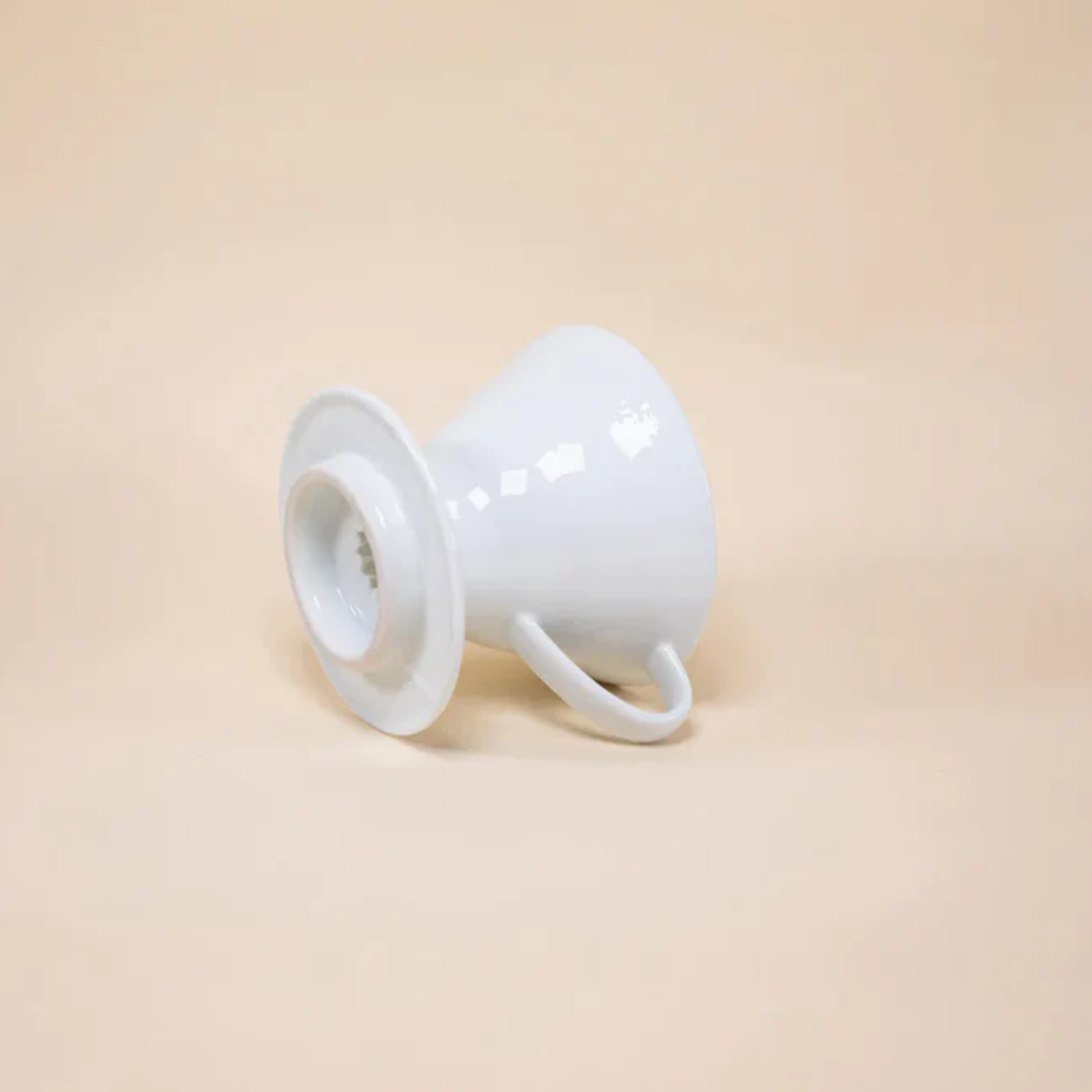 Laid and showing the bottom part of HARIO V60 ceramic coffee dripper white porcelain with spiral ridges and conical shape for adjustable brewing flow, includes polypropylene measuring spoon.