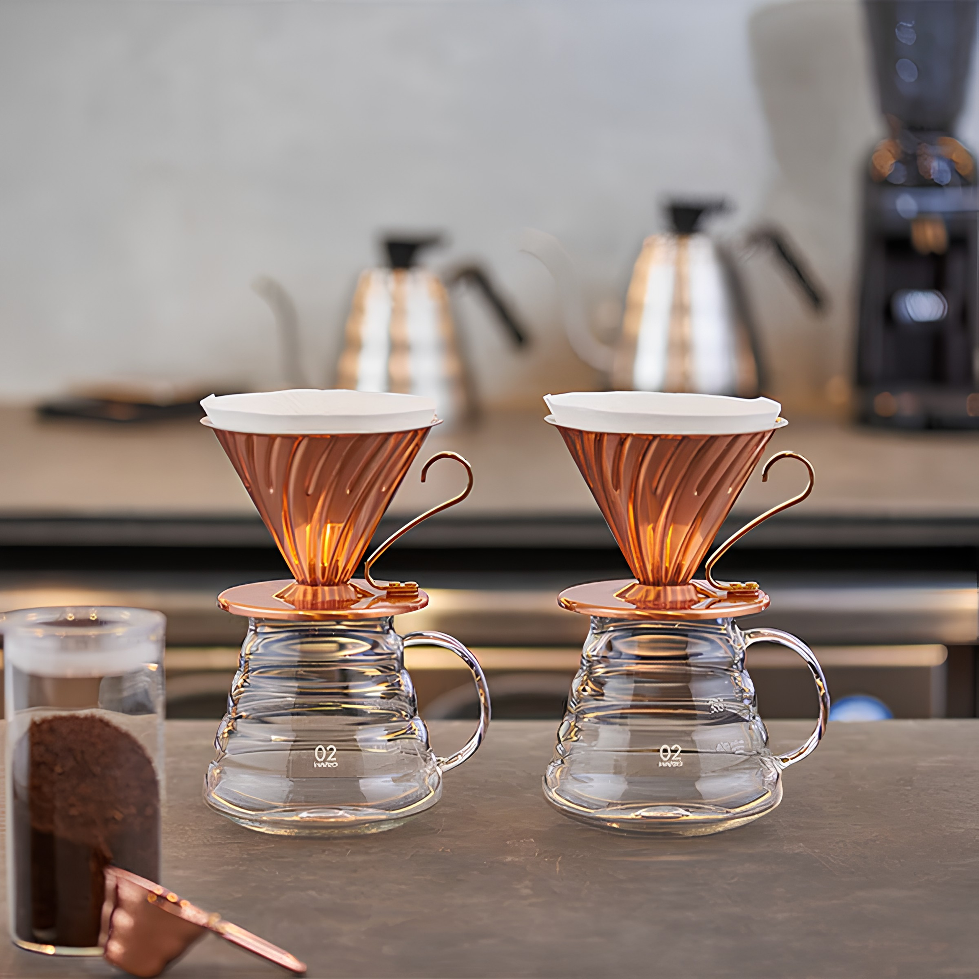 Two Hario V60 Copper Coffee Dripper 02 placed on glass servers. It has a capacity of 1-4 cups, and weighs approximately 300g, featuring heat distribution evenly and antibacterial property of copper, widely used for kitchenware.