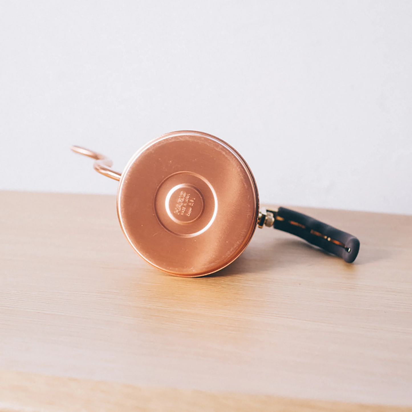 Bottom view with the Hario logo from the Hario V60 Drip Kettle Buono 700ml Copper which includes Body of kettle and lid from copper, nickel and sealed with baked coating, lid knob from natural wood, handle from brass and handle cover from silicone rubber, luxurious of all kettles, iconic shape.