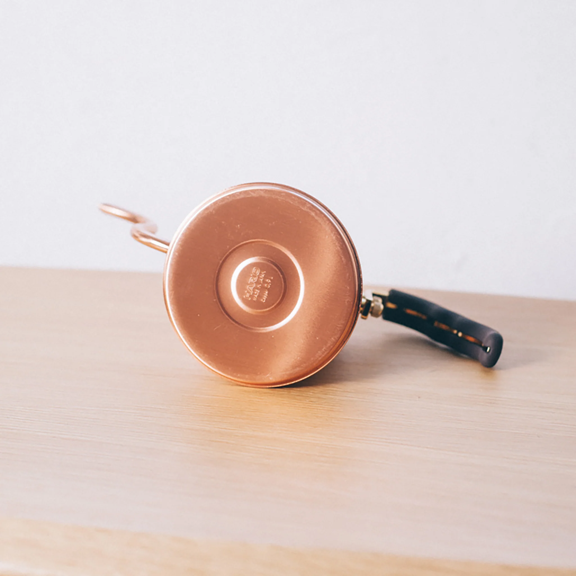 Bottom view with the Hario logo from the Hario V60 Drip Kettle Buono 700ml Copper which includes Body of kettle and lid from copper, nickel and sealed with baked coating, lid knob from natural wood, handle from brass and handle cover from silicone rubber, luxurious of all kettles, iconic shape.