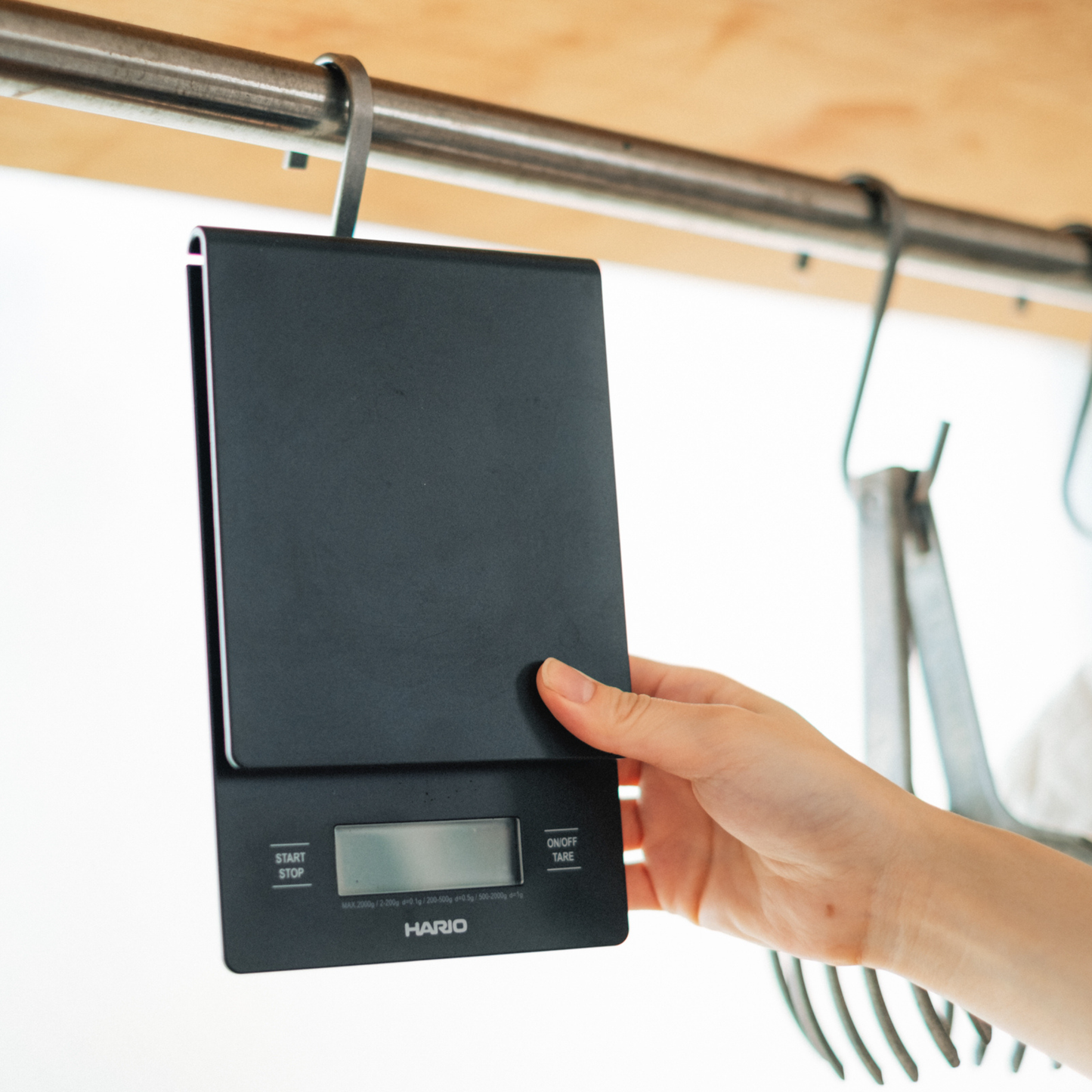 HARIO V60 Drip Scale Black, shown being hanged by a hook, ABS resin with built-in timer and precision measurement up to 2000 grams.