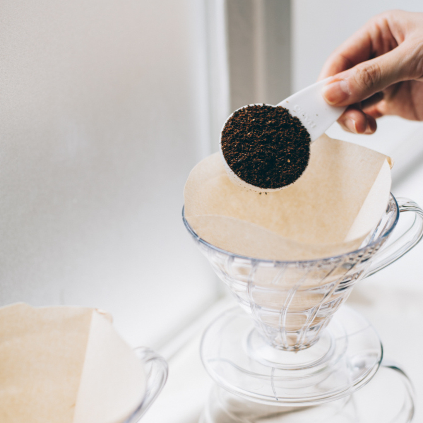 Shown coffee being put in the HARIO V60 coffee paper filters 02 natural brown unbleached paper pulp designed for V60 drippers for clear and balanced coffee, 1 to 4 cup capacity.