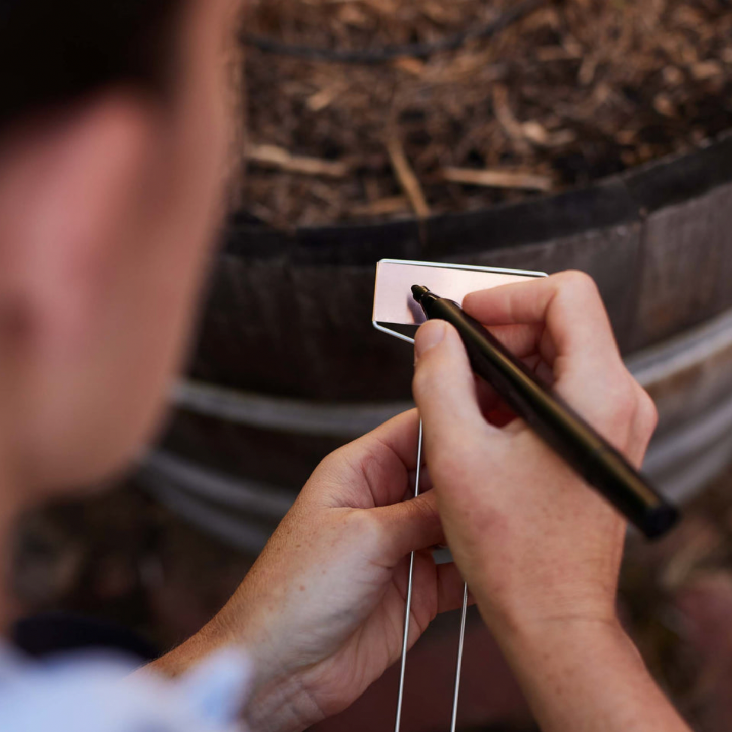 Person using marker to label Heaven in Earth Garden Labels Copper (pack of 10) with dirt barrel 