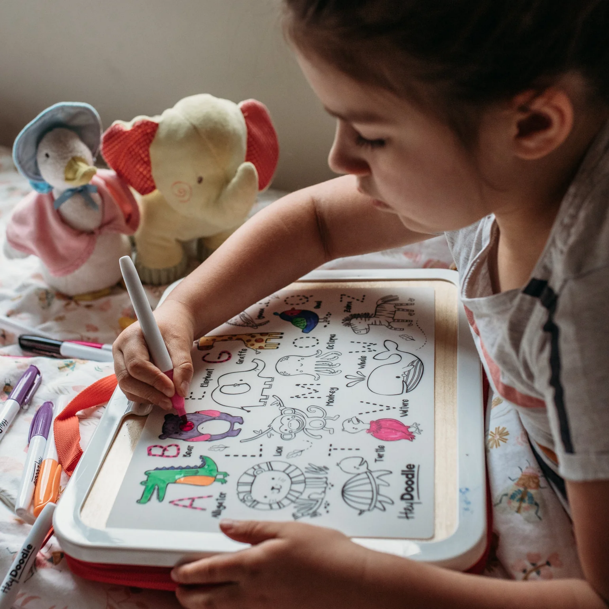 Young girl drawing and writing with Hey Doodle matt on bed
