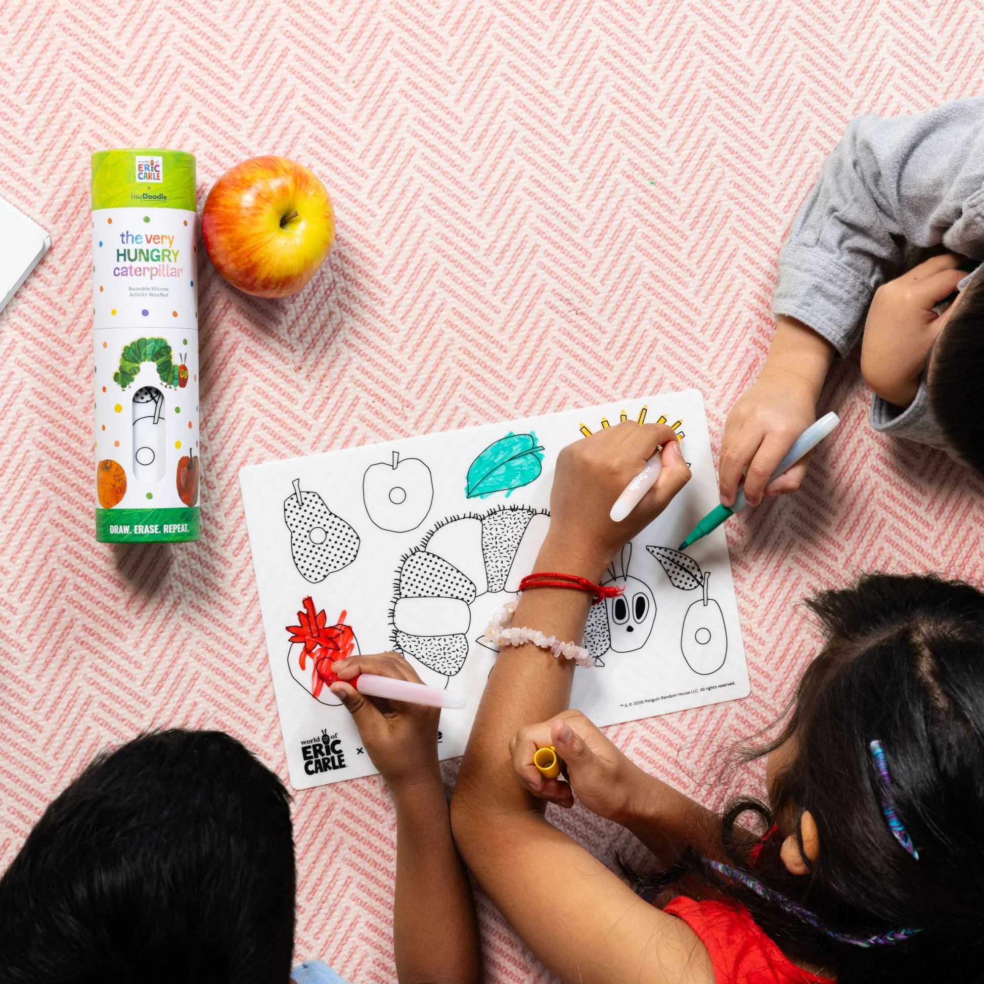 Three children color a The Very Hungry Caterpillar sheet with markers beside the Hey Doodle Mini Colouring & Doodle Mat.