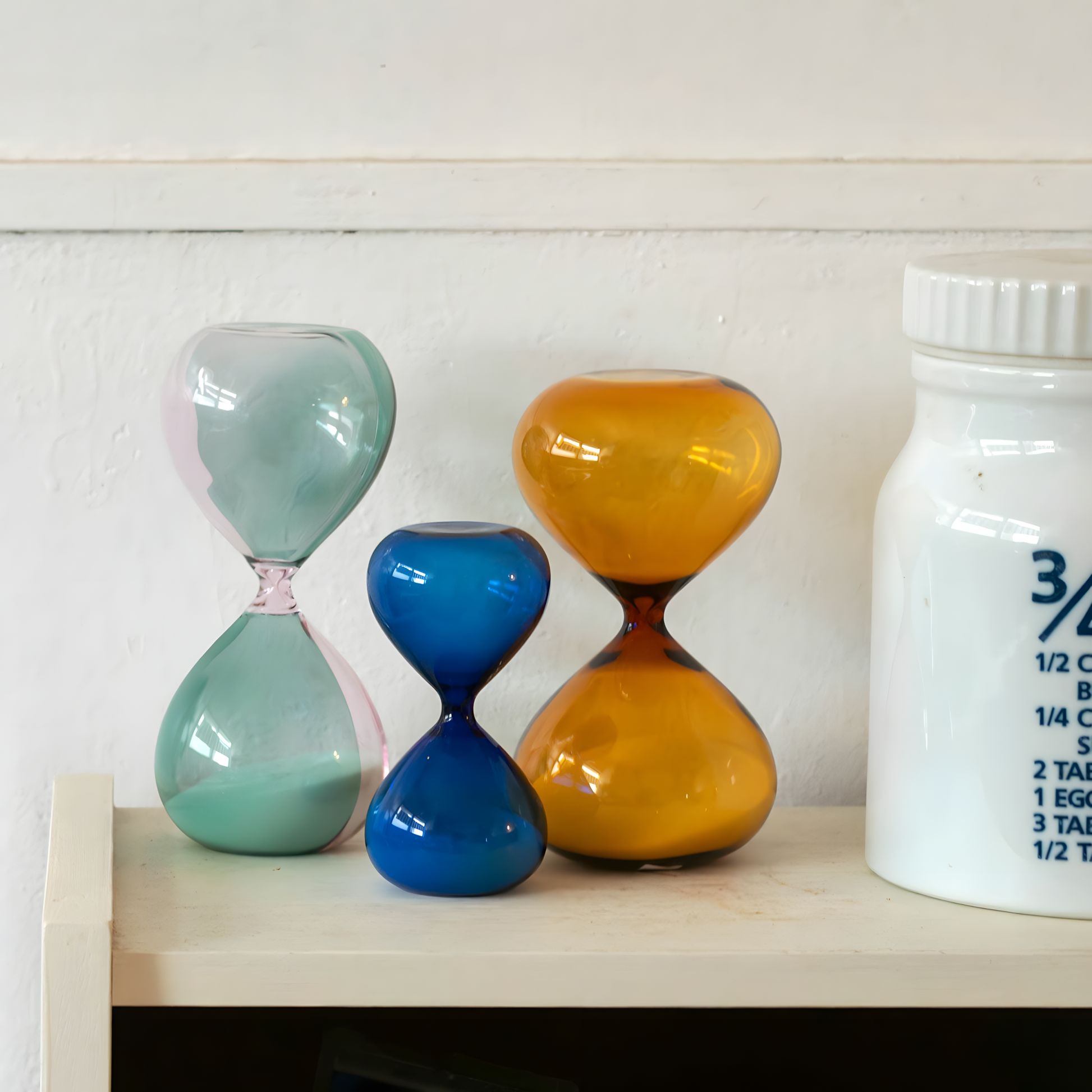 Showing other different hourglass sizes with Hightide large hourglass featuring amber glass and coloured sand, offering a 15-minute timer for work sessions, relaxing breaks, or decorative home styling. A modern glass hourglass perfect for shelves, offices, and creative spaces.