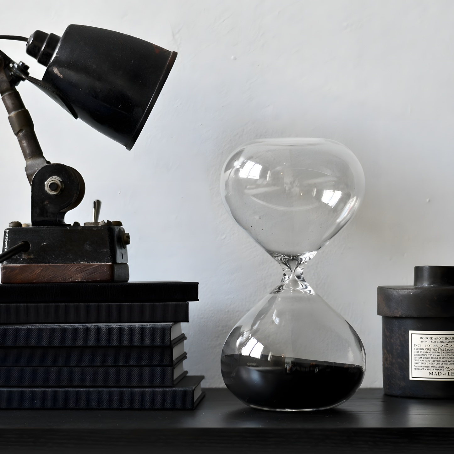 Shown beside a pile of books, Hightide extra-large hourglass with clear glass and coloured sand, designed as a 30-minute sand timer for longer focus sessions, home décor, or kitchen use. A striking, handmade glass hourglass that enhances any workspace or room.