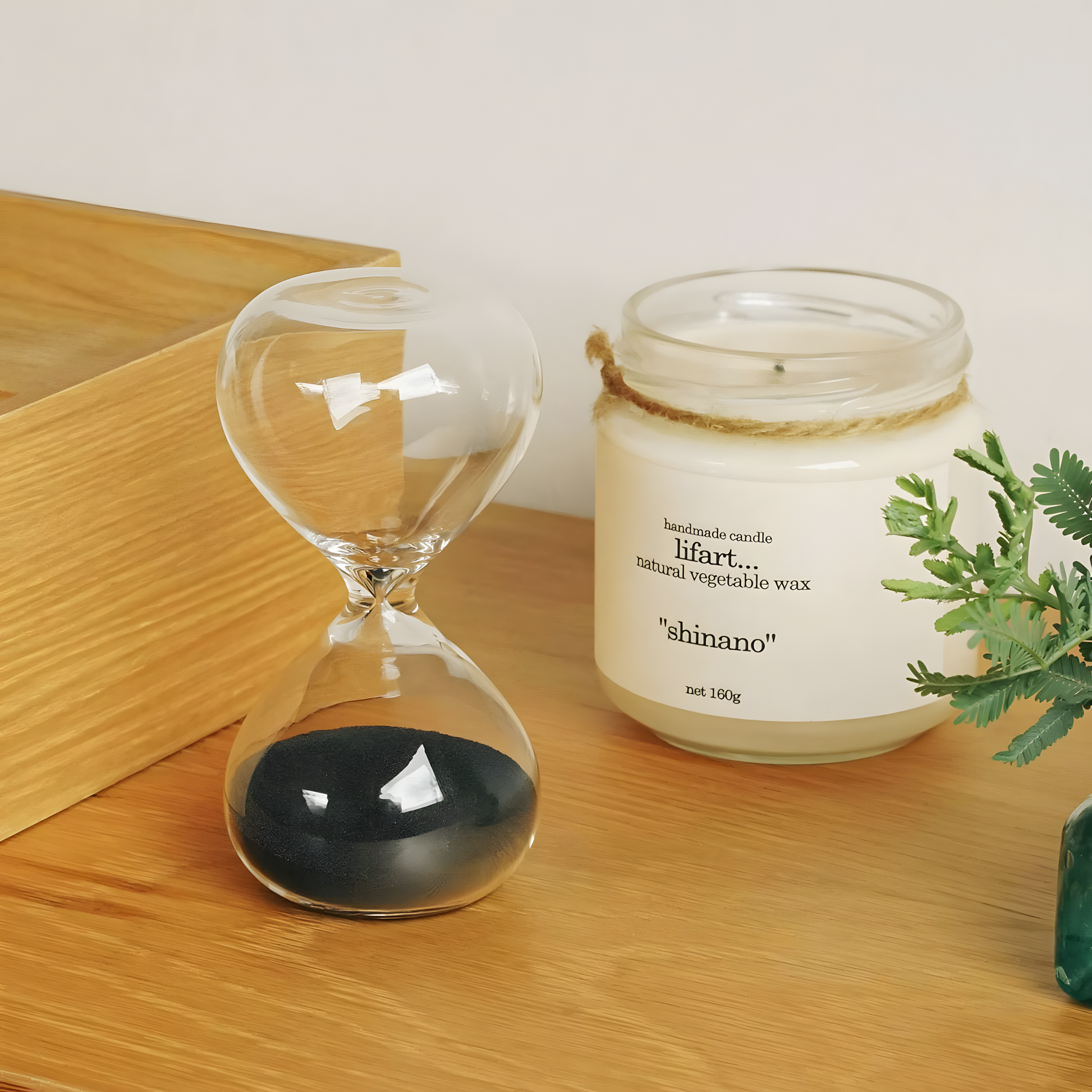 Shown on a table with a bottle of candle wax beside it, Hightide medium hourglass with clear glass and coloured sand, a 5-minute handmade sand timer ideal for productivity, cooking, meditation, or desk décor. Stylish Japanese-designed hourglass for everyday timing needs.
