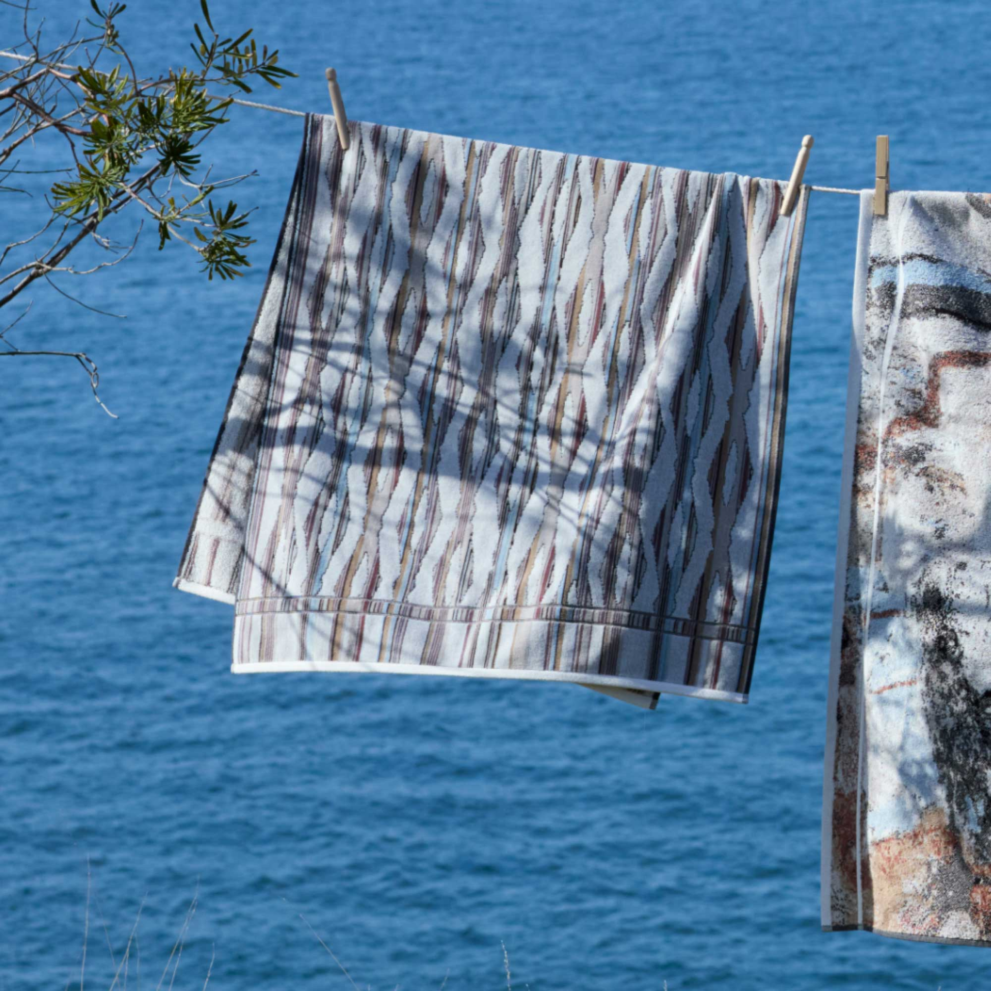 The Innate Ripple Light Bath Towel 70cm x 140cm hung on a clothesline outside - Misty Grey and White - 100% OEKO-TEX® Certified Cotton - Absorbent velour and terry bath towel with soft ripple breeze pattern, responsibly woven in Portugal for everyday use.