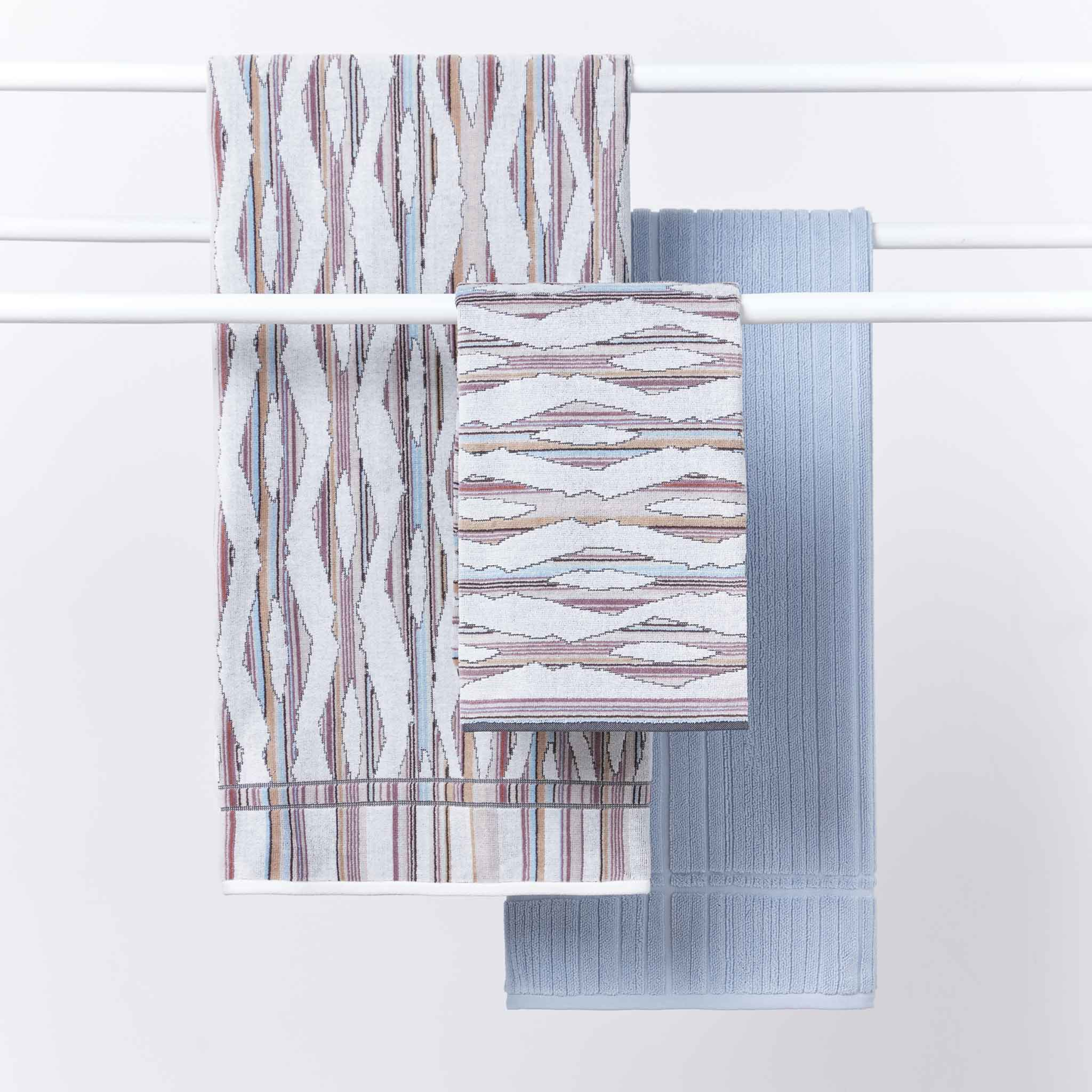 Shown hung on a clothesline with the other bigger towels, the Ripple Light Hand Towel 40cm x 70cm - Misty Grey and White - 100% OEKO-TEX® Certified Cotton - Absorbent velour and terry jand towel with soft ripple breeze pattern, responsibly woven in Portugal for everyday use.