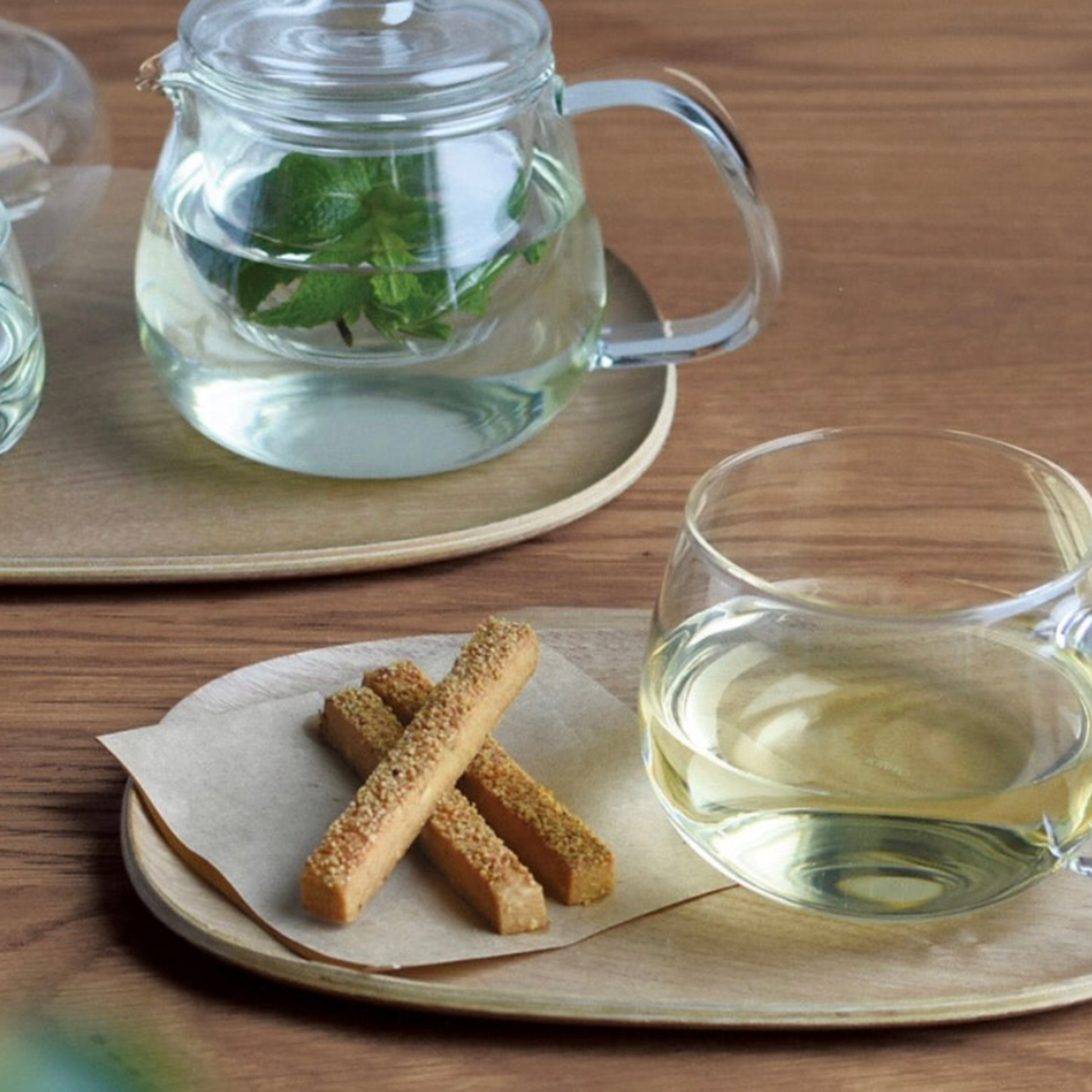 Stylish glass Kinto Unitea Cup 350ml filled with tea being served with biscuits and teapot 