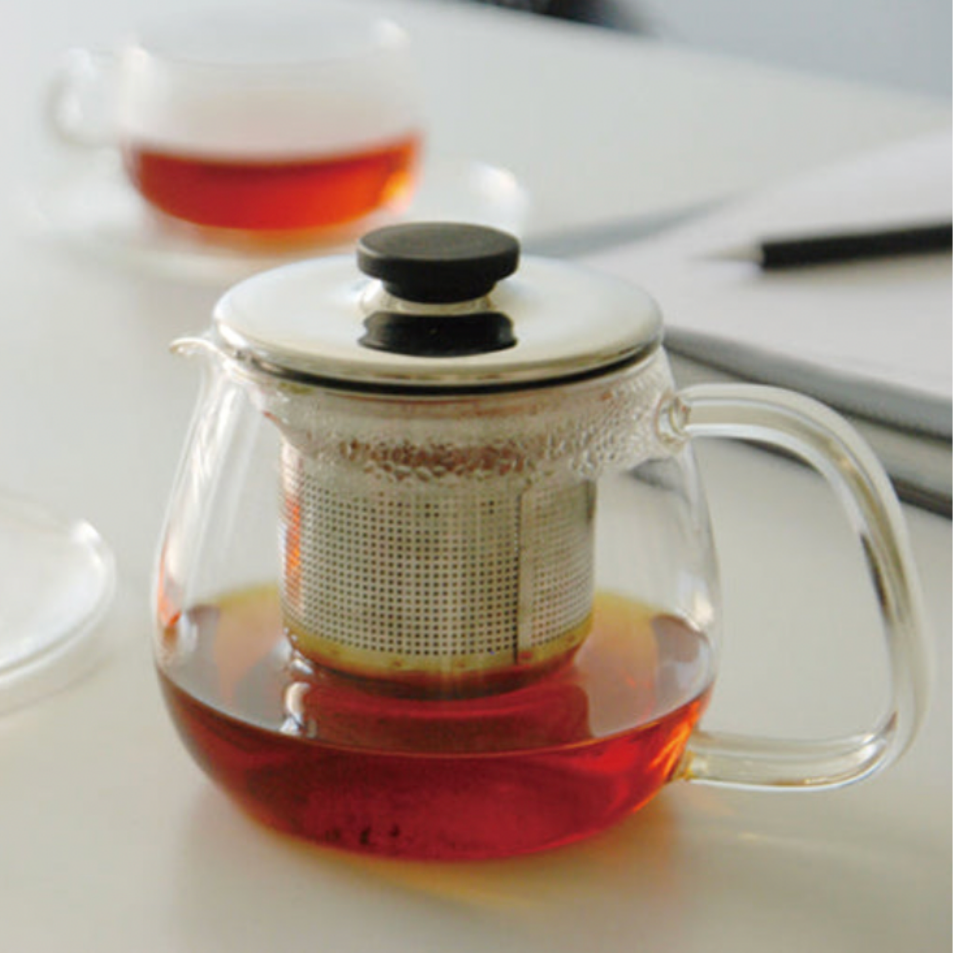 Stylish glass Kinto Unitea Teapot 500ml with stainless steel strainer and lid on display with other Kinto glassware on a desk with tea 