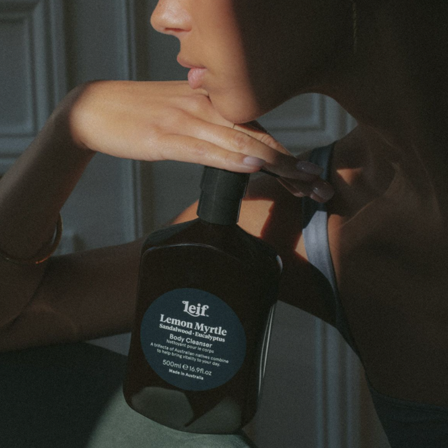 Woman posing with her hand to her chin holding Leif body cleanser Lemon Myrtle 500ml on couch in house setting 