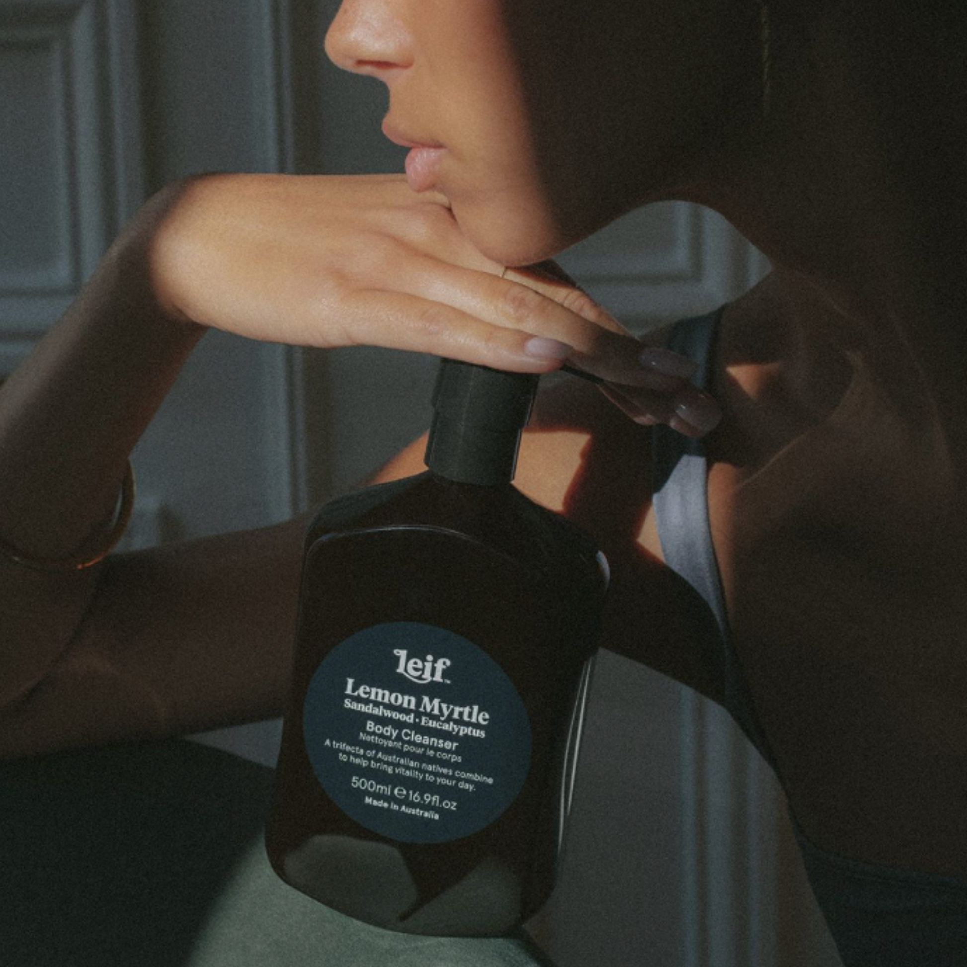 Woman posing with her hand to her chin holding Leif body cleanser Lemon Myrtle 500ml on couch in house setting 