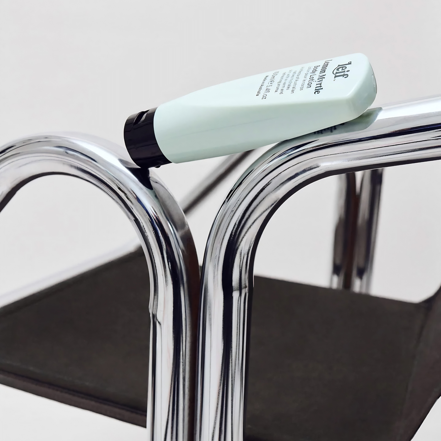 Side view of the Leif Body Lotion 100ml Lemon Myrtle on a chair, it is warm and herbaceous with sandalwood and eucalyptus, in a design fit for travel.