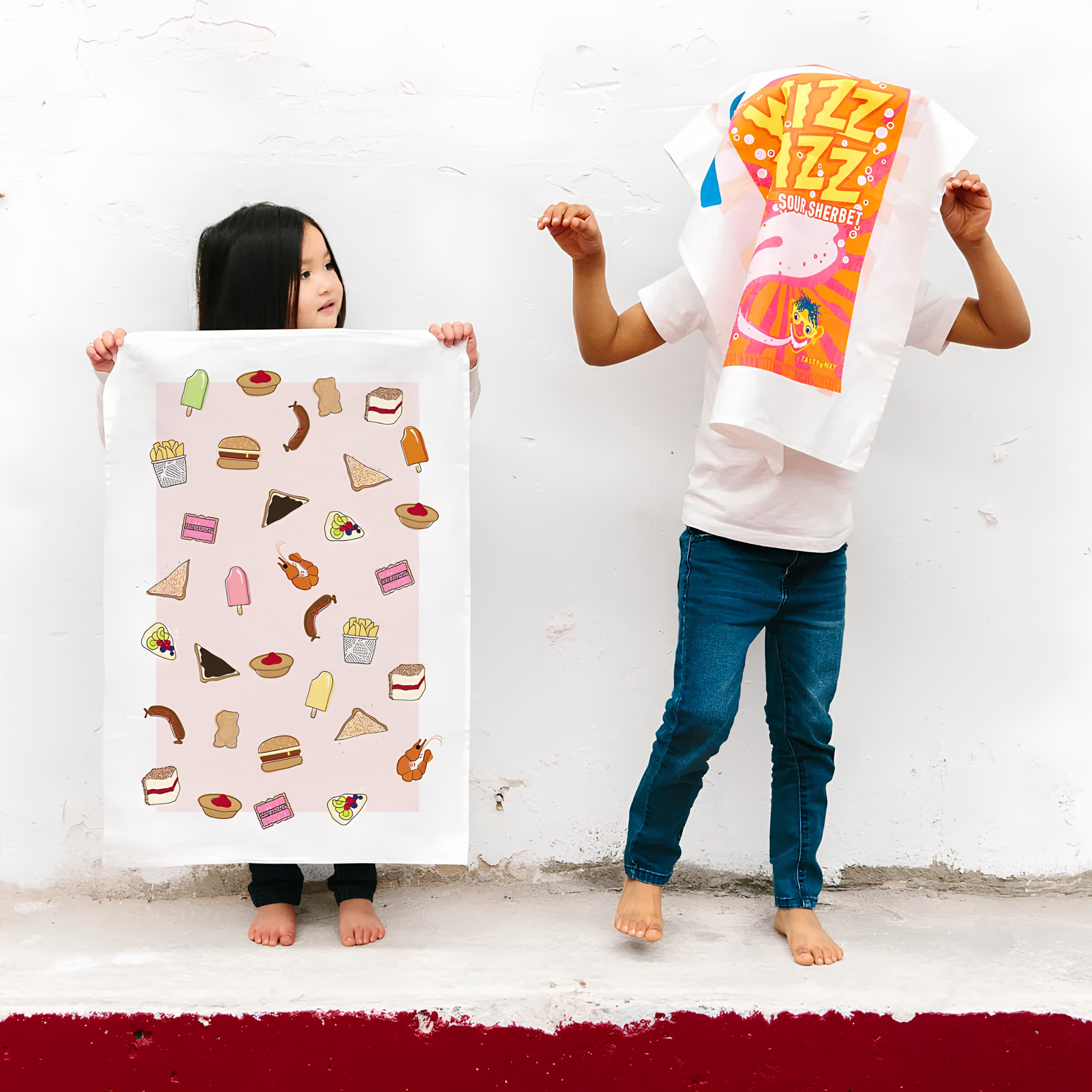 A girl holding the front of the Make Me Iconic Tea Towel Aussie Foods, images of food that fills lunchboxes or late-night cravings put in a tea towel made from high quality, absorbent fabric.