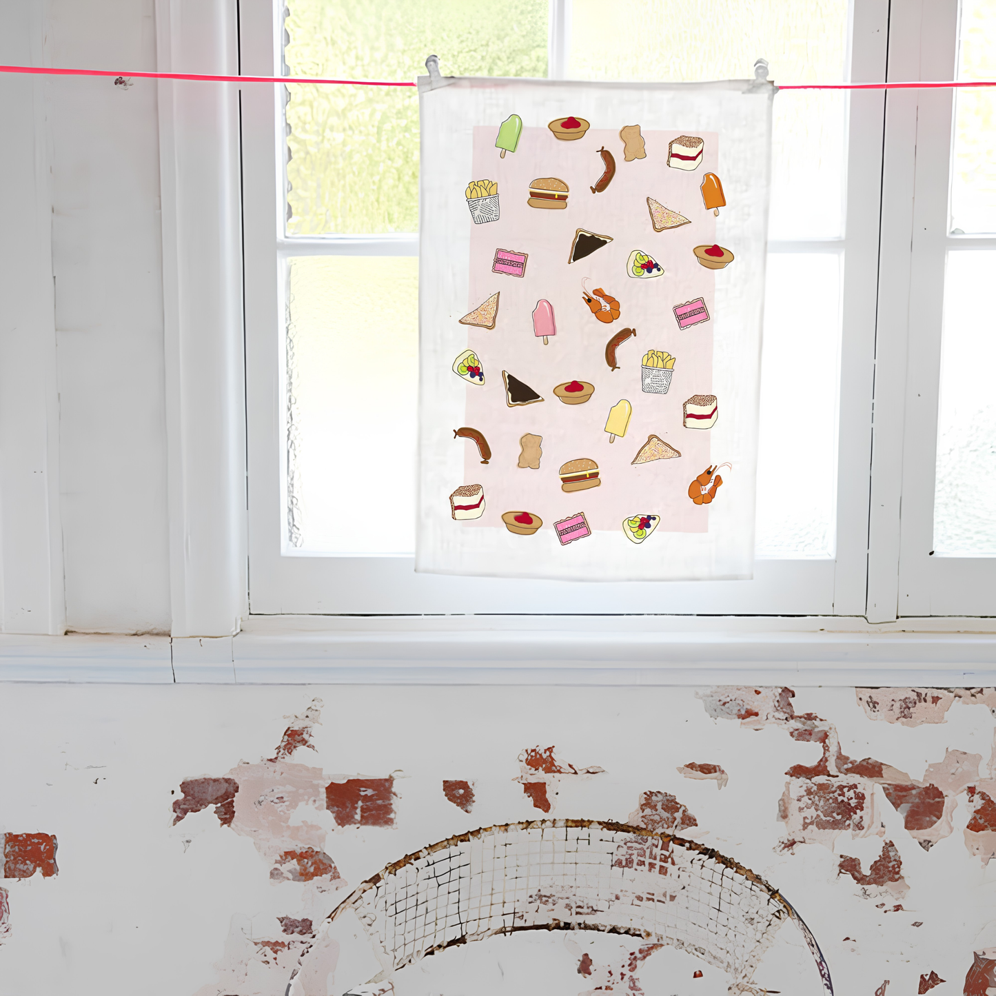 Shown hung near the window, the Make Me Iconic Tea Towel Aussie Foods, images of food that fills lunchboxes or late-night cravings put in a tea towel made from high quality, absorbent fabric.