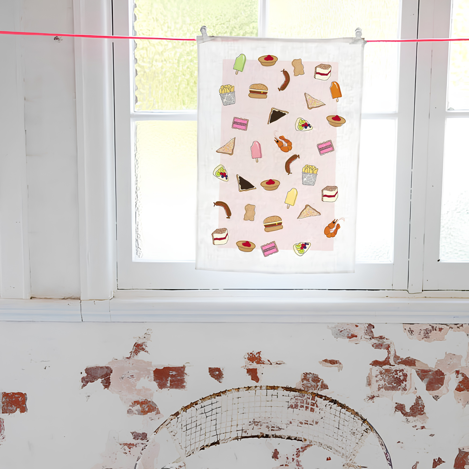Shown hung near the window, the Make Me Iconic Tea Towel Aussie Foods, images of food that fills lunchboxes or late-night cravings put in a tea towel made from high quality, absorbent fabric.