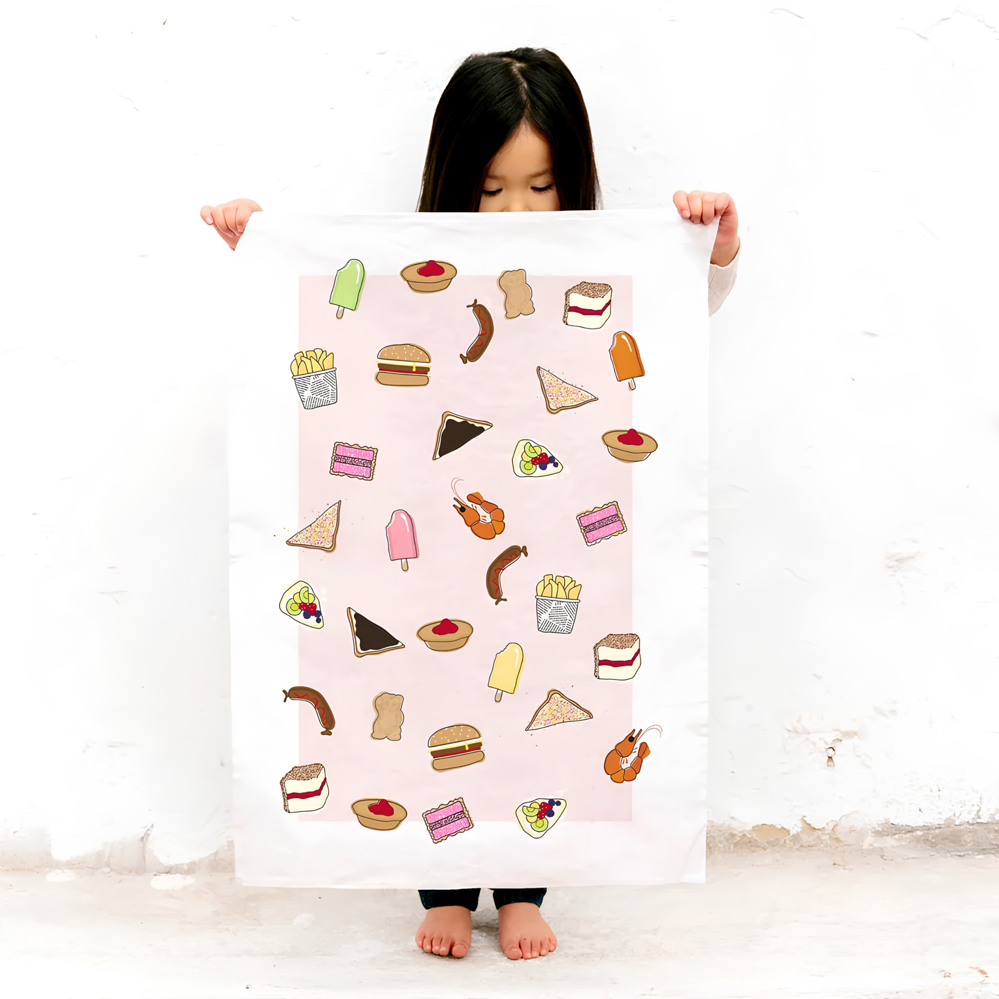 Another photo of a girl holding the Make Me Iconic Tea Towel Aussie Foods, images of food that fills lunchboxes or late-night cravings put in a tea towel made from high quality, absorbent fabric.