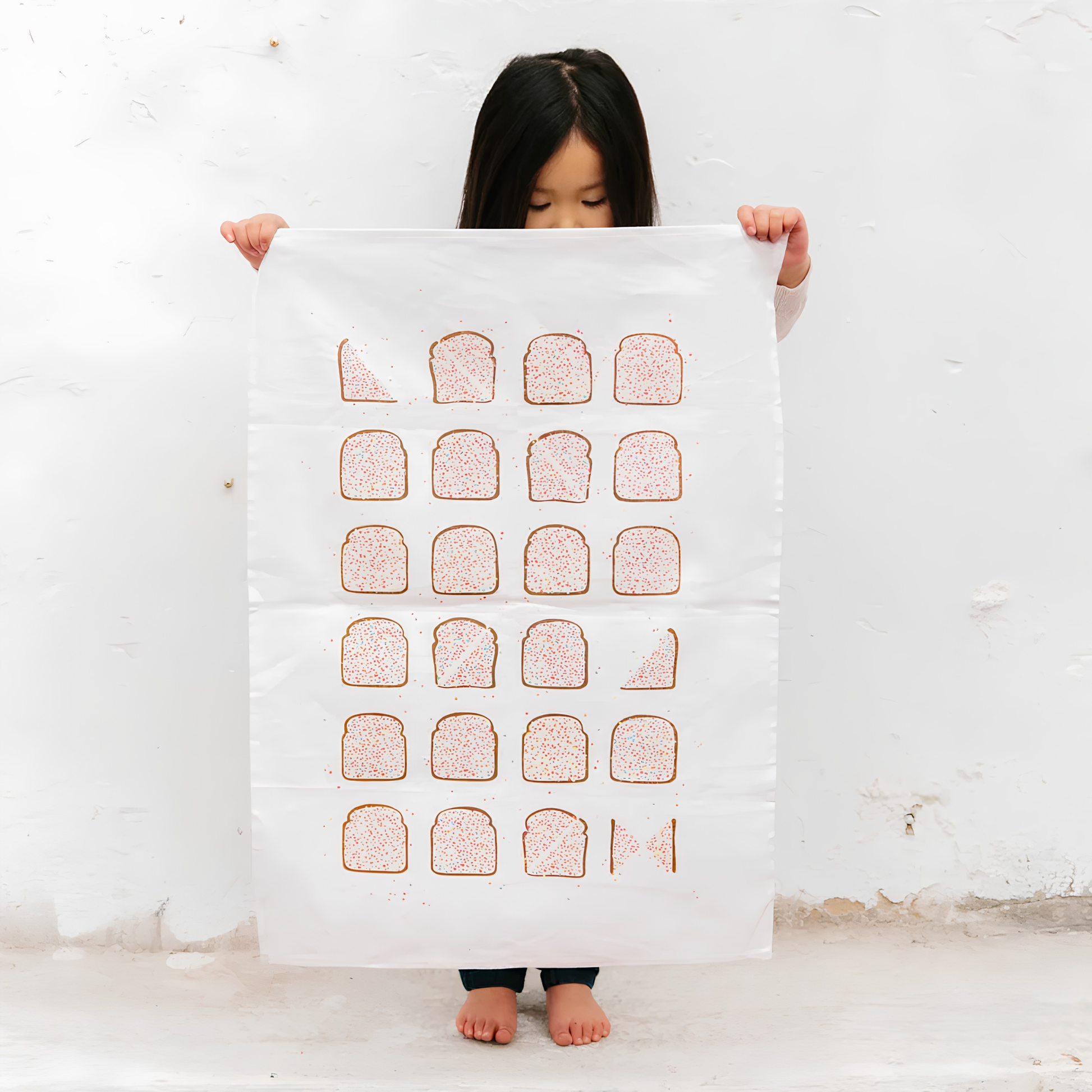 A little girl holding the front of the Make Me Iconic Tea Towel Fairy Bread, one of Australia's most iconic treats, these slices of bread with butter and rainbow sprinkles put on a tea towel. Made from high quality, absorbent fabric.
