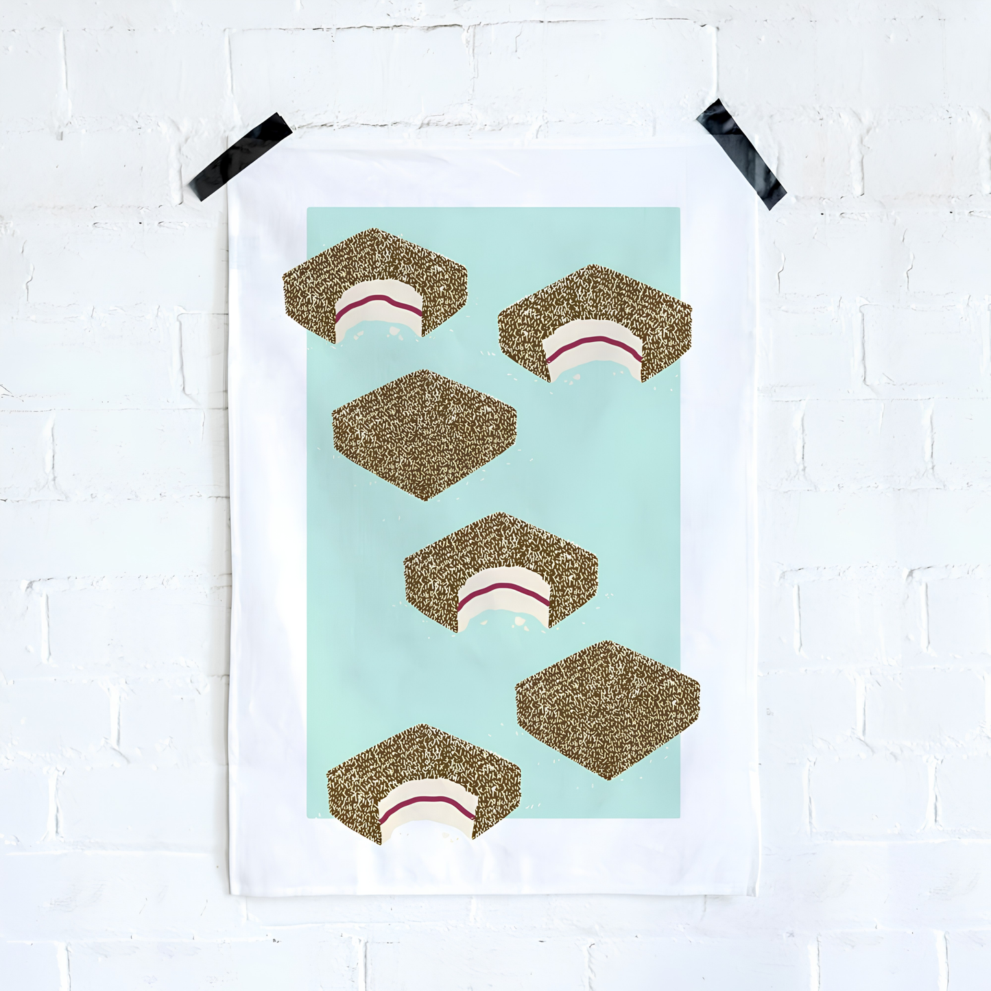 Make Me Iconic Lamington Tea Towel taped on the wall, featuring Australia's classic chocolate-coated, coconut-covered treat. Made from high-quality, absorbent fabric.