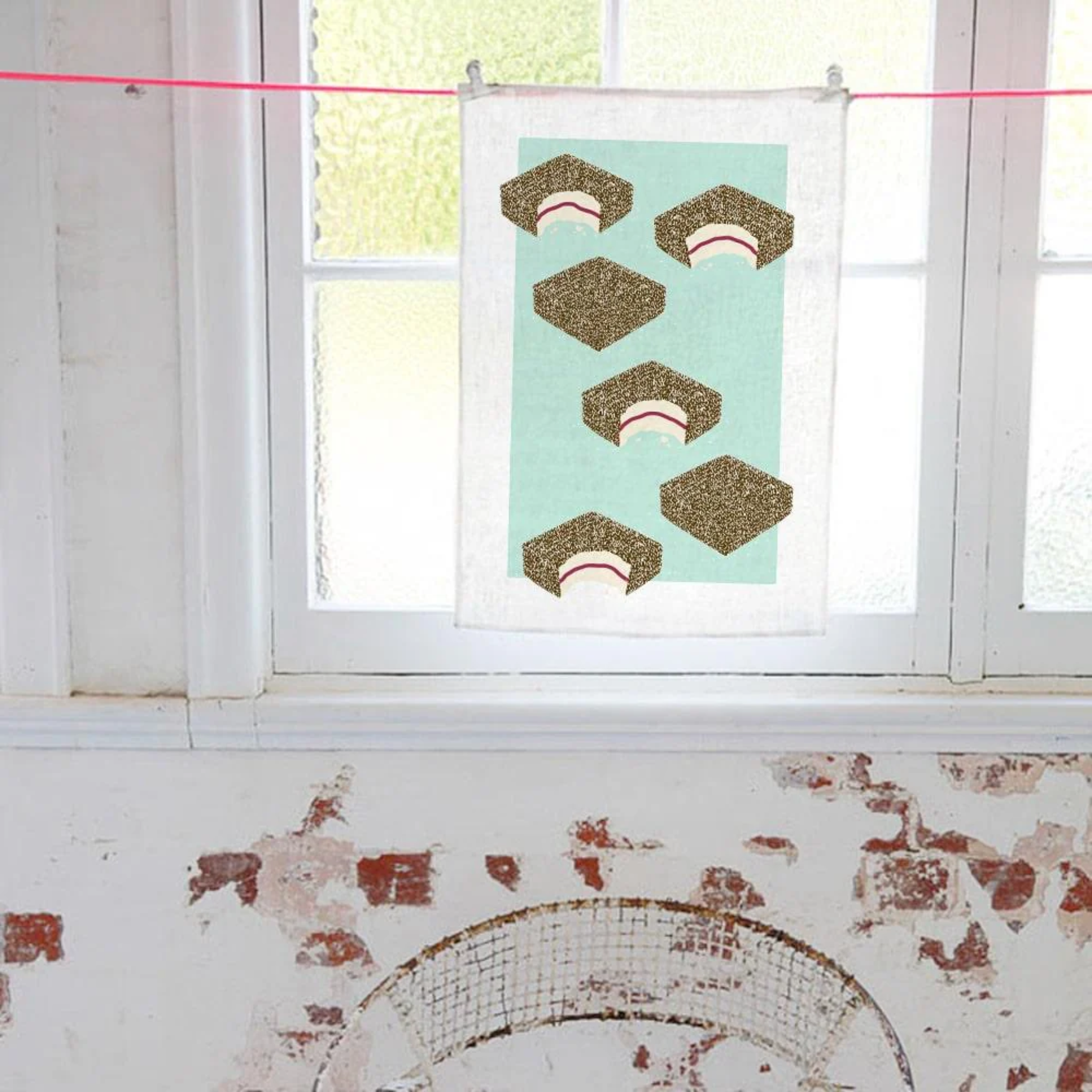 Hung inside near the window, the Make Me Iconic Lamington Tea Towel featuring Australia's classic chocolate-coated, coconut-covered treat. Made from high-quality, absorbent fabric.