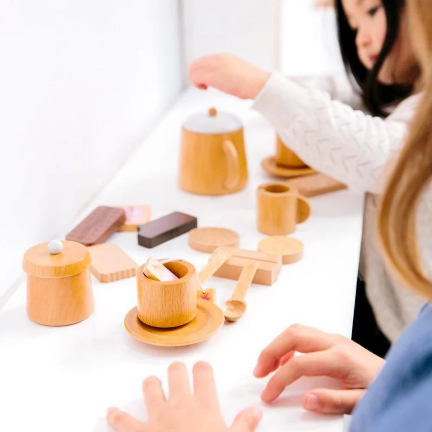 Little girls playing on a table Make Me Iconic wooden Australian biscuit toy set featuring 10 classic Arnott's-style biscuits with numbers on the back, handcrafted from non-toxic wood and stored in a decorative tin - perfect for pretend tea parties and playful learning with Aussie charm.