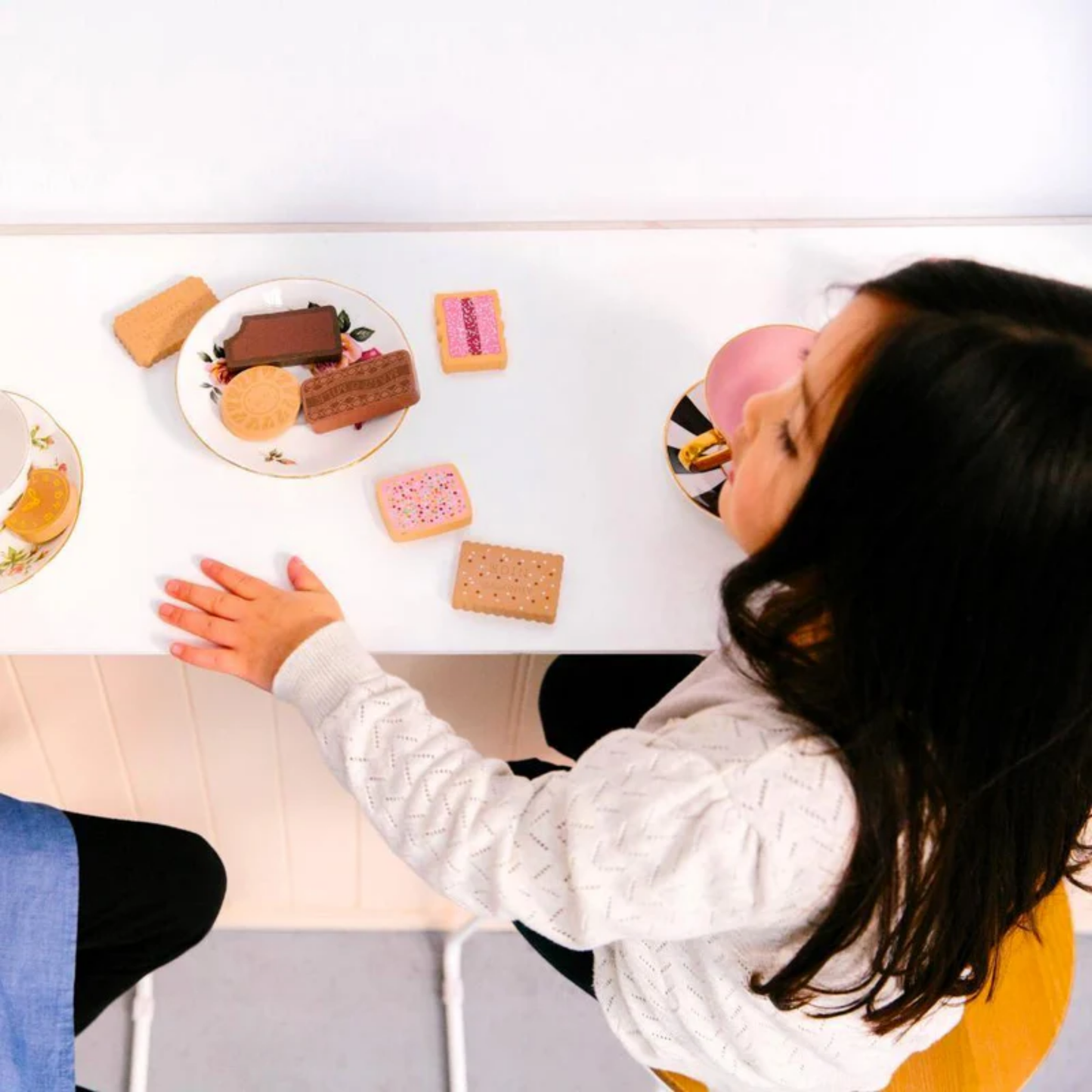 Little girls playing on a table showing the wooden biscuits of Make Me Iconic wooden Australian biscuit toy set featuring 10 classic Arnott's-style biscuits with numbers on the back, handcrafted from non-toxic wood and stored in a decorative tin - perfect for pretend tea parties and playful learning with Aussie charm.