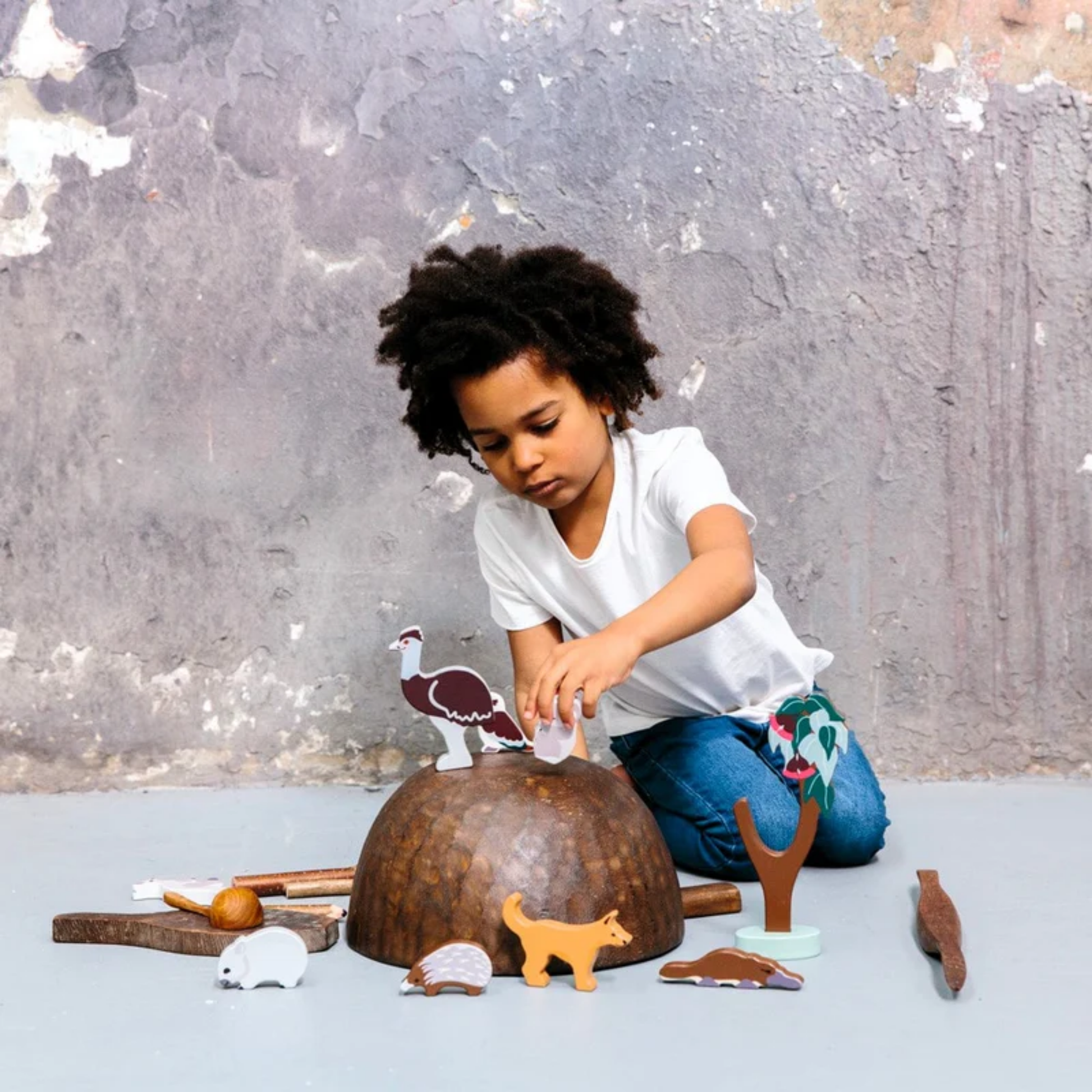 A little boy playing the Make Me Iconic wooden Australian animal toy set featuring eight native animals and a gum tree, crafted from non-toxic wood with eco packaging - includes kangaroo, koala, wombat, platypus, emu, echidna, dingo, and kookaburra for open-ended play celebrating Aussie wildlife and culture.