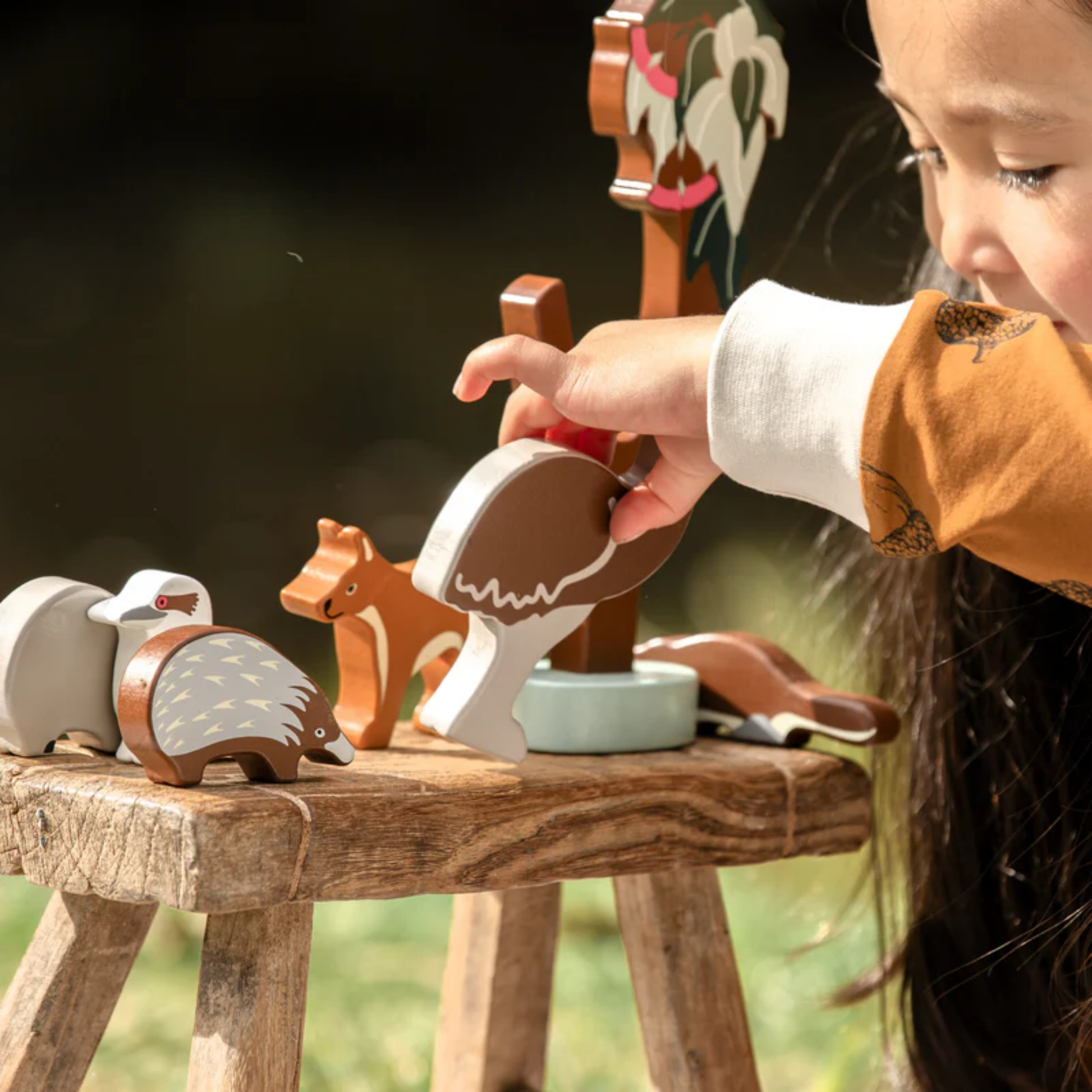 A litte girl playing the wooden toys from Make Me Iconic wooden Australian animal toy set featuring eight native animals and a gum tree, crafted from non-toxic wood with eco packaging - includes kangaroo, koala, wombat, platypus, emu, echidna, dingo, and kookaburra for open-ended play celebrating Aussie wildlife and culture.