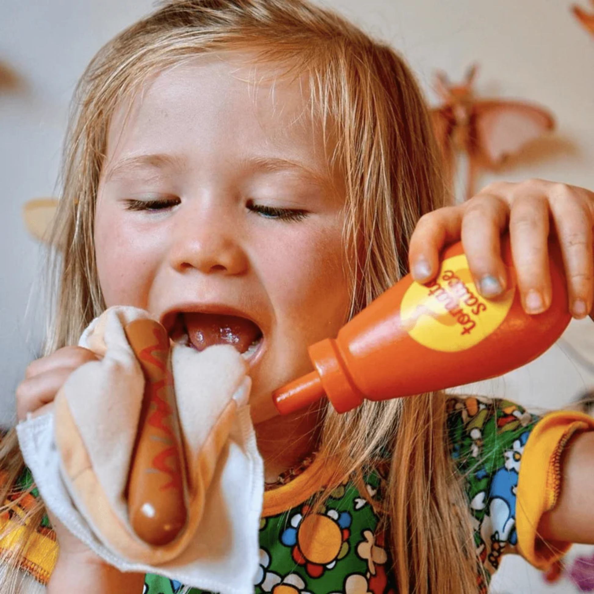 Little girl playing sausage and bread from Make Me Iconic wooden Aussie food toy set featuring 38 handcrafted pieces including classic favourites like sausage sandwich, burger, lamington, meat pie, fairy bread, and chips, made from non-toxic wood with felt and Velcro parts - perfect for pretend barbecues, kitchen play, and creative Aussie-themed fun.