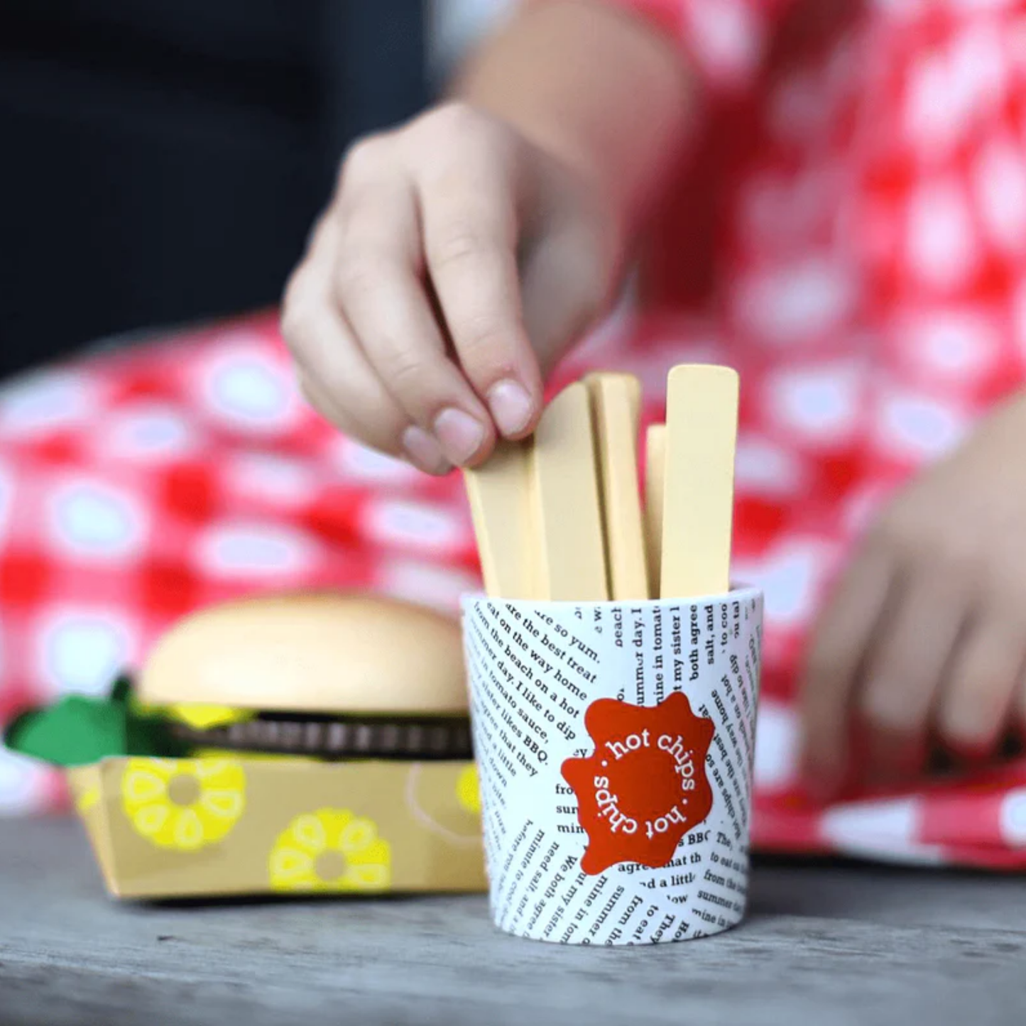 Little girl playing burger and fries toys from Make Me Iconic wooden Aussie food toy set featuring 38 handcrafted pieces including classic favourites like sausage sandwich, burger, lamington, meat pie, fairy bread, and chips, made from non-toxic wood with felt and Velcro parts - perfect for pretend barbecues, kitchen play, and creative Aussie-themed fun.