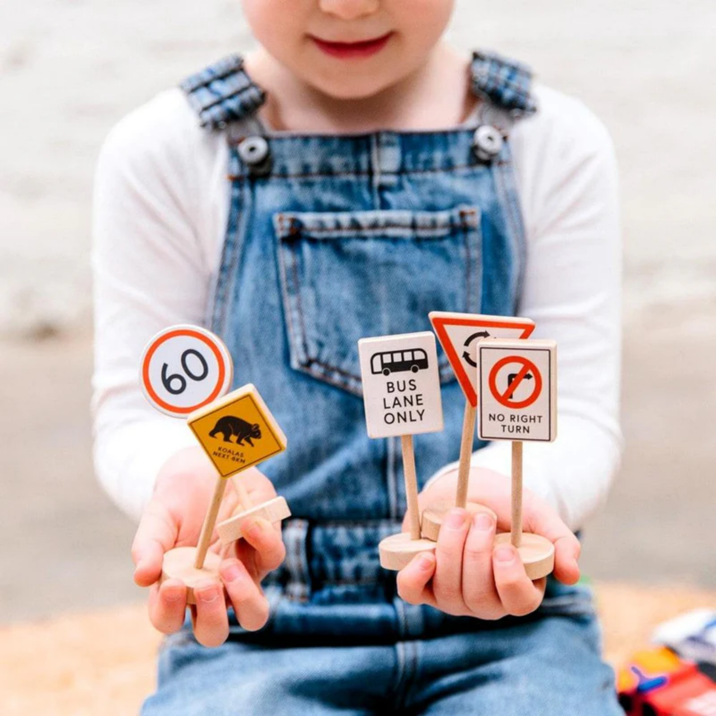 Showing a kid holding the Make Me Iconic wooden traffic sign play set - multicolor solid wood toy featuring 5 double-sided Australian road signs for imaginative and educational car play.