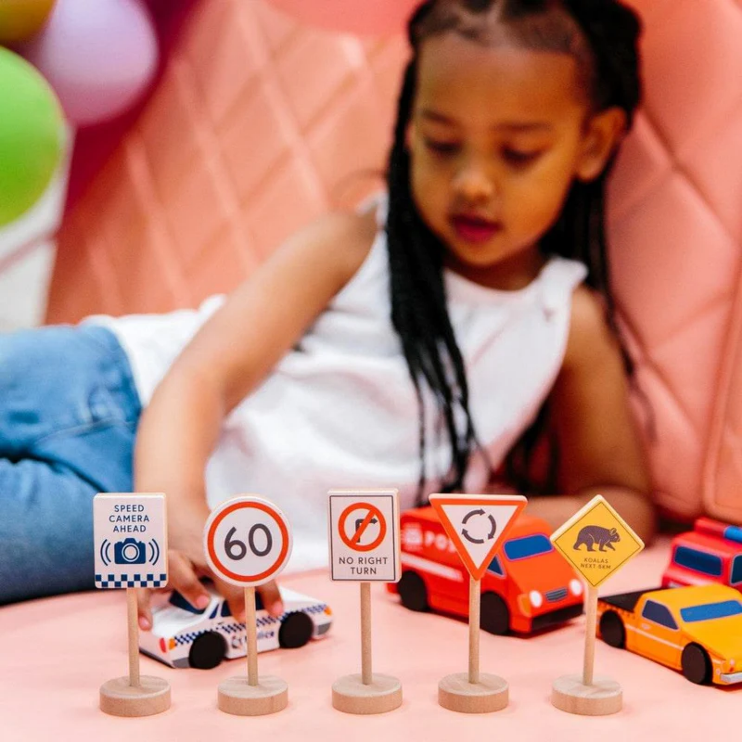 Little girl playing cars and road signs from Make Me Iconic wooden traffic sign play set - multicolor solid wood toy featuring 5 double-sided Australian road signs for imaginative and educational car play.