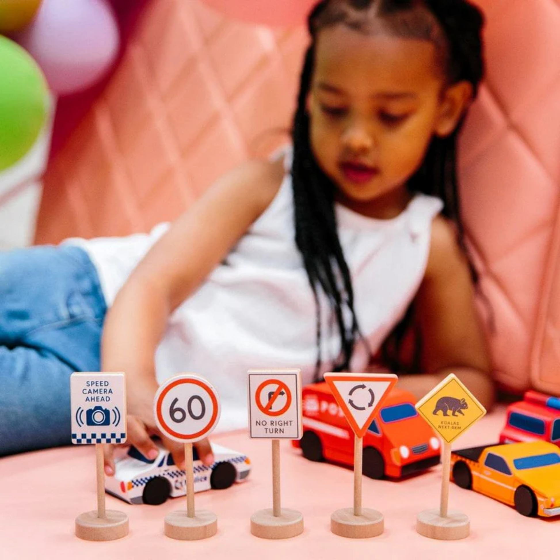 Little girl playing cars and road signs from Make Me Iconic wooden traffic sign play set - multicolor solid wood toy featuring 5 double-sided Australian road signs for imaginative and educational car play.