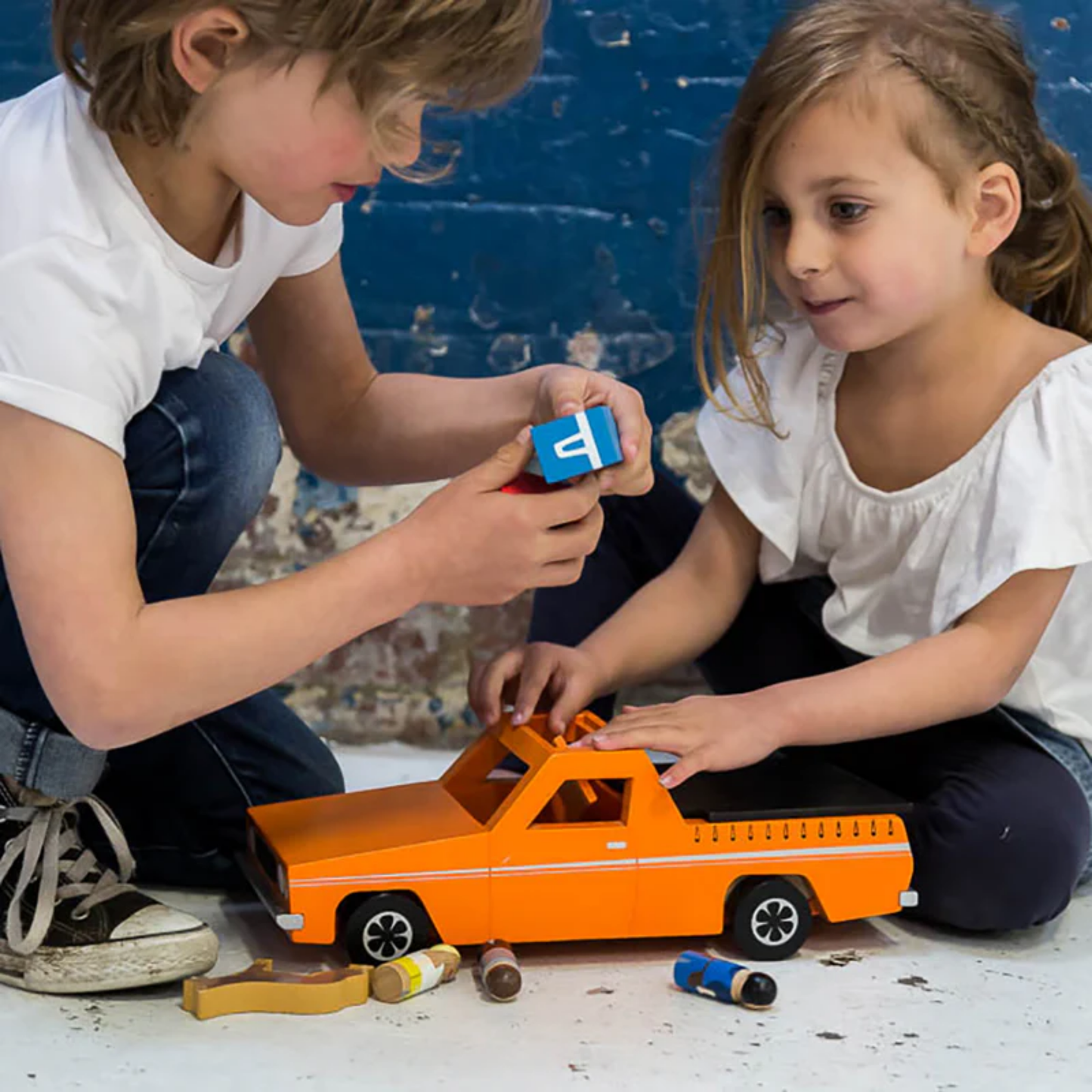 Kids playing Make Me Iconic wooden blue Ute toy set with rolling wheels, lift-off roof, three wooden passengers, a Kelpie dog, surfboard, esky, and toolbox - a nostalgic Aussie-inspired playset designed in Australia to spark creativity and hands-on imaginative fun for children aged 3 and up.