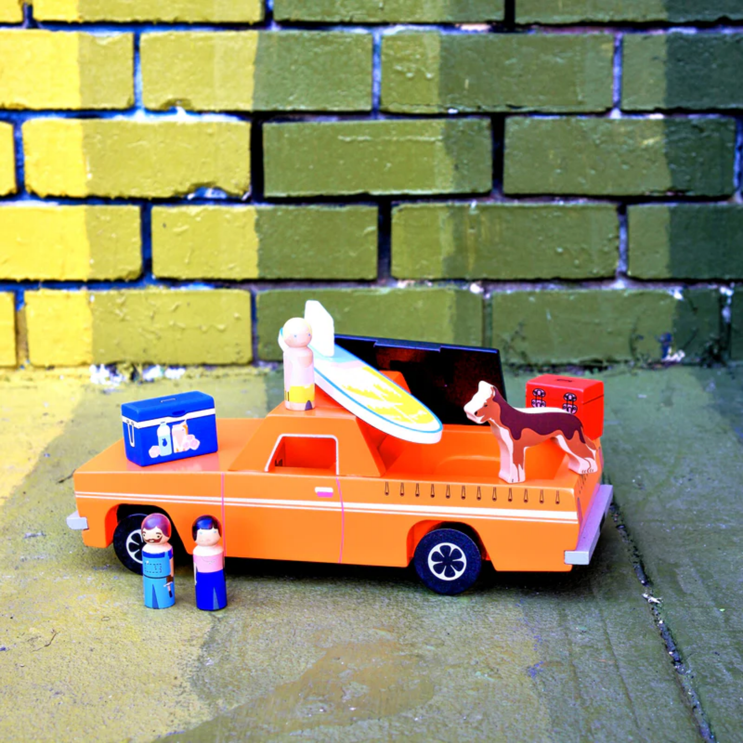 Shown on the floor Make Me Iconic wooden blue Ute toy set with rolling wheels, lift-off roof, three wooden passengers, a Kelpie dog, surfboard, esky, and toolbox - a nostalgic Aussie-inspired playset designed in Australia to spark creativity and hands-on imaginative fun for children aged 3 and up.