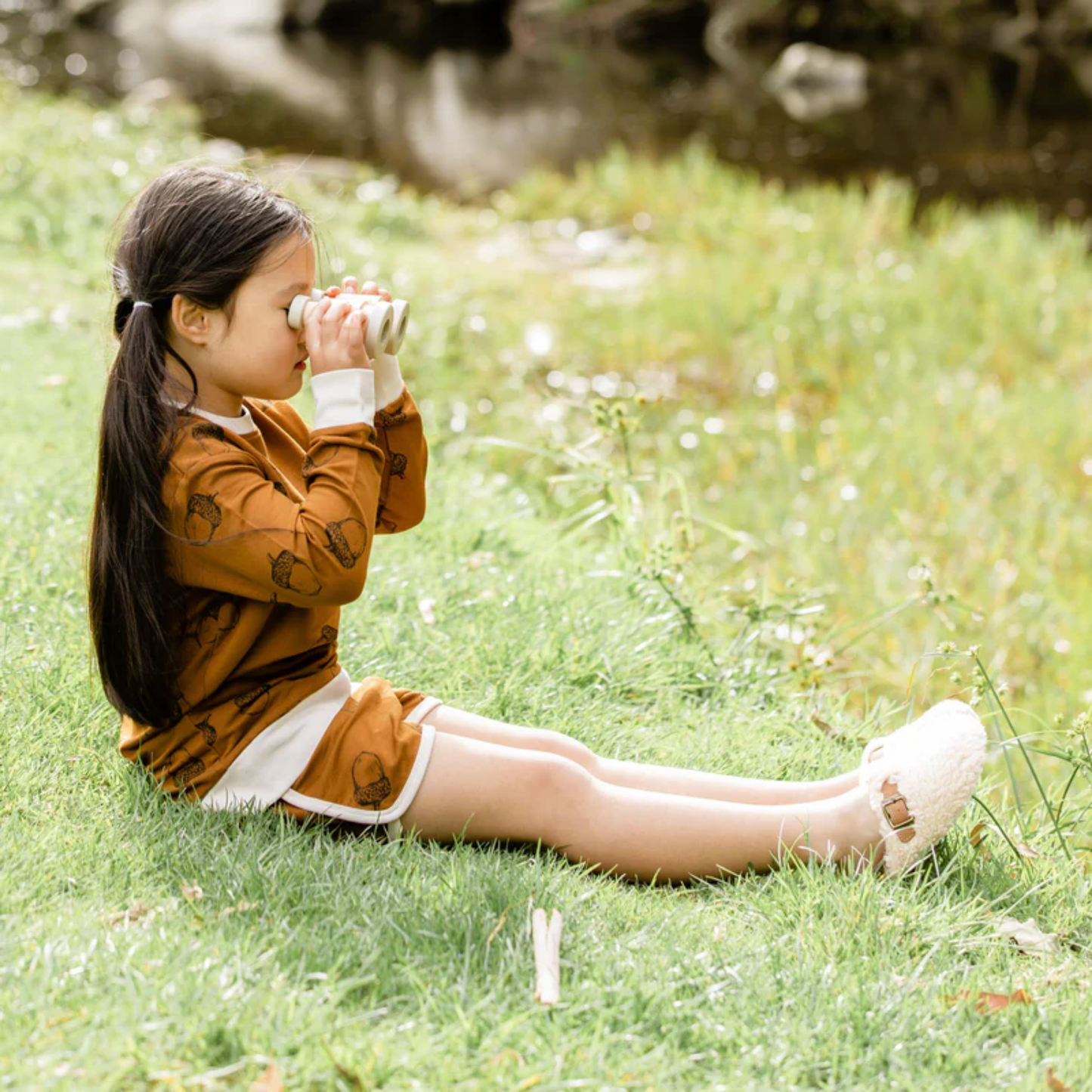 Little girl using the Make Me Iconic wooden toy binoculars - natural solid wood binoculars designed for kids' imaginative play, featuring a smooth finish and easy-grip shape for little explorers.