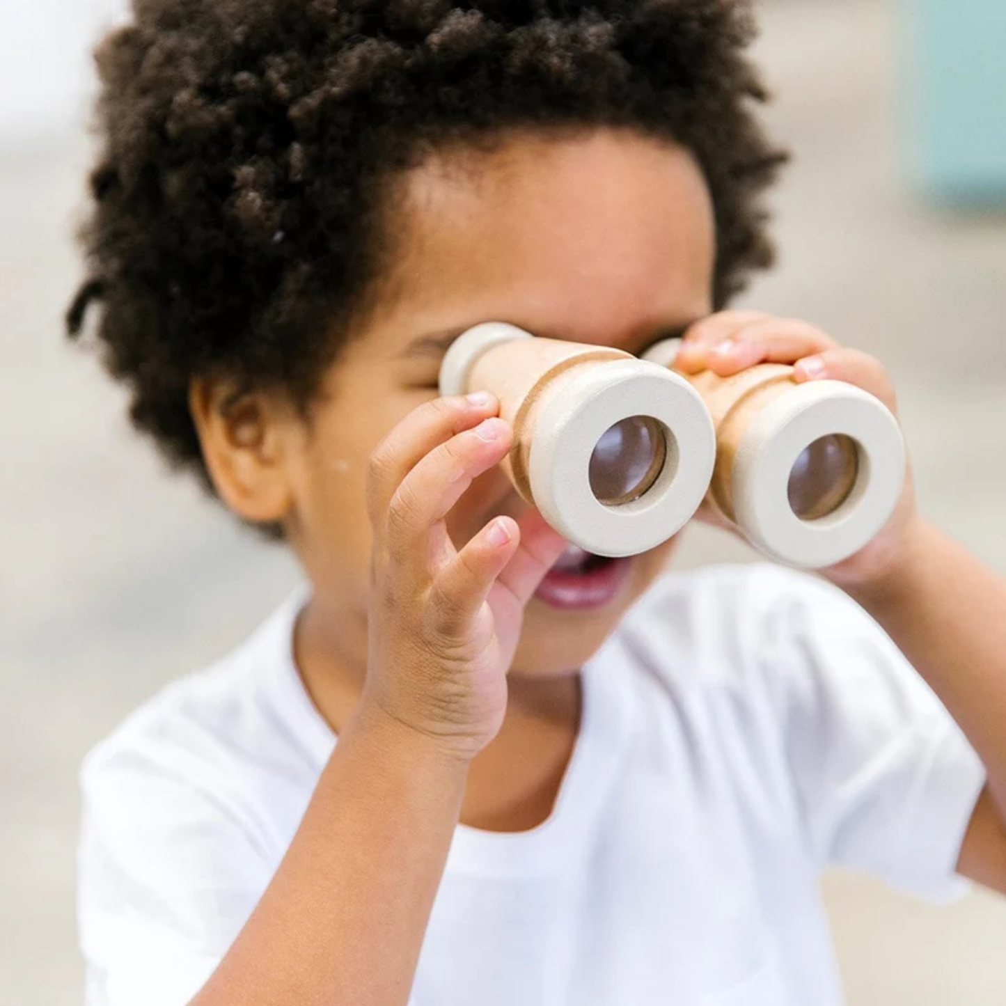 Little boy using the Make Me Iconic wooden toy binoculars - natural solid wood binoculars designed for kids' imaginative play, featuring a smooth finish and easy-grip shape for little explorers.