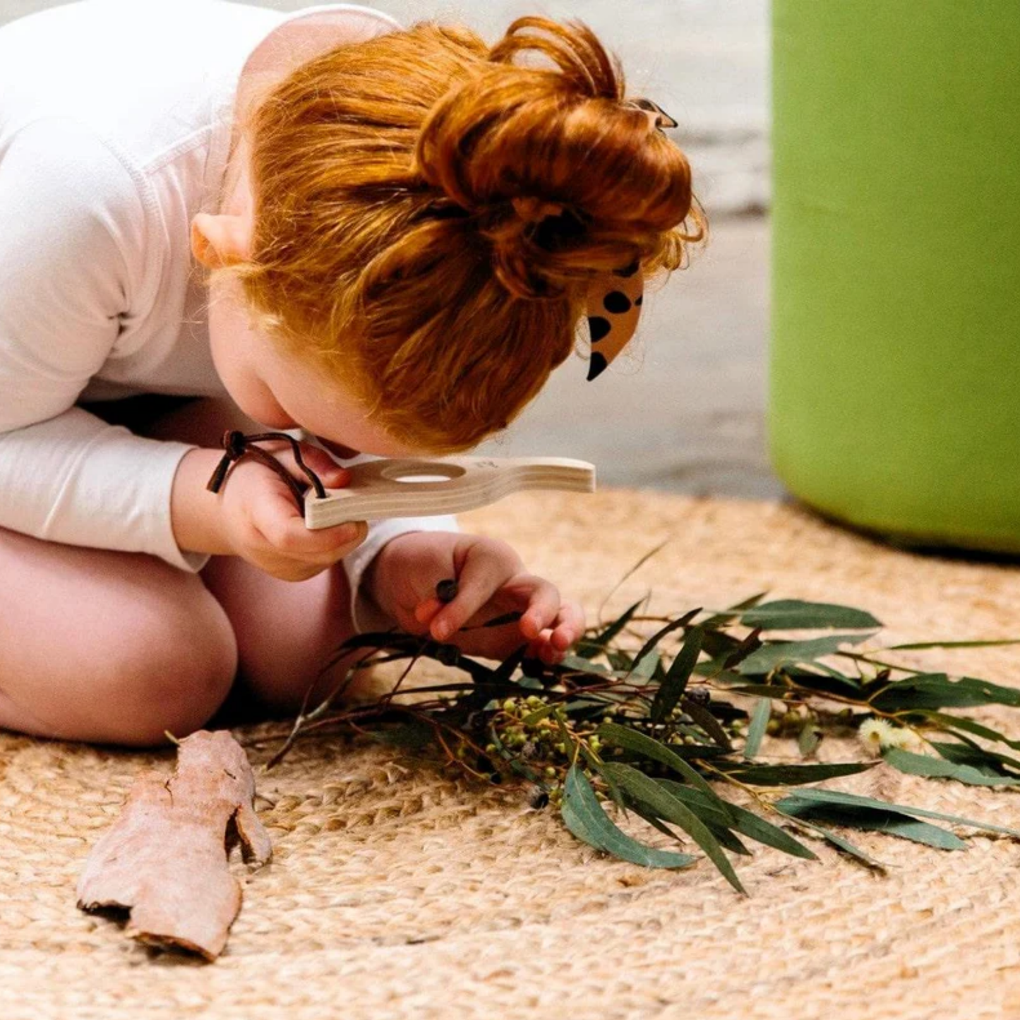 Showing a girl magnifying a plant using Make Me Iconic Leaf Magnify Glass - Green wooden magnifying toy for kids, made from sturdy wood with a safe plastic lens and carry loop for outdoor exploration.