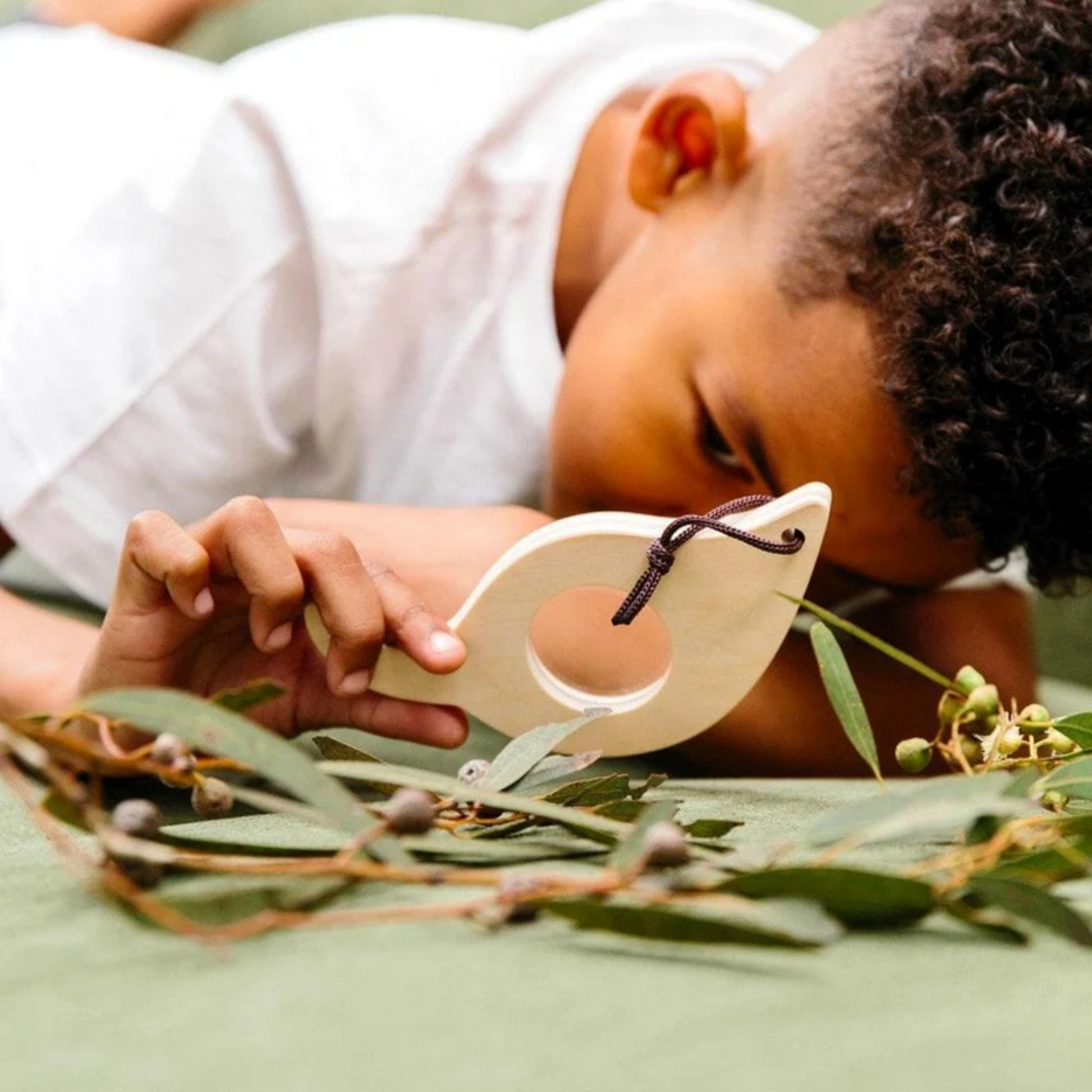 A boy magnifying a plant using Make Me Iconic Leaf Magnify Glass - Green wooden magnifying toy for kids, made from sturdy wood with a safe plastic lens and carry loop for outdoor exploration.